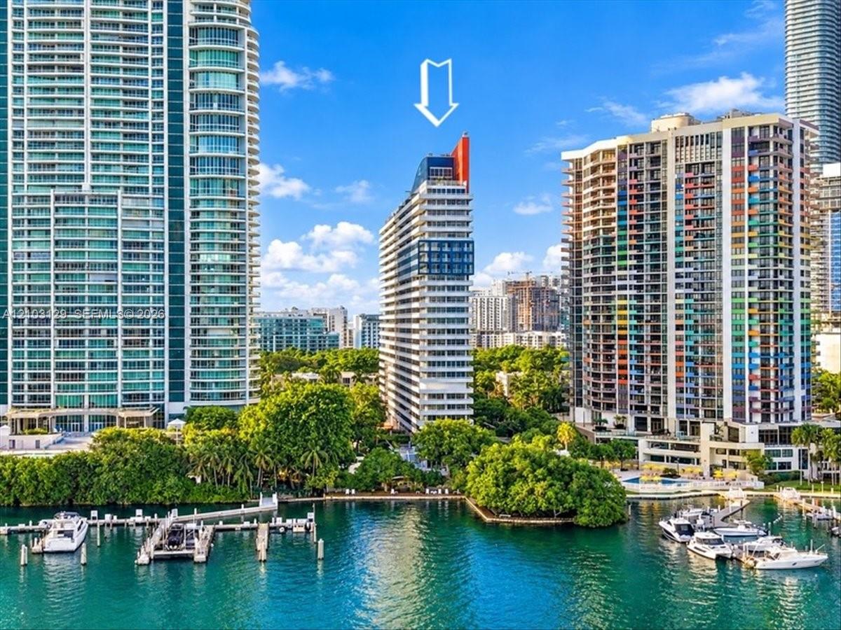 High-rise residential building featuring expansive glass paneling, a distinctive architectural roofline, white exterior facade, and direct water frontage
