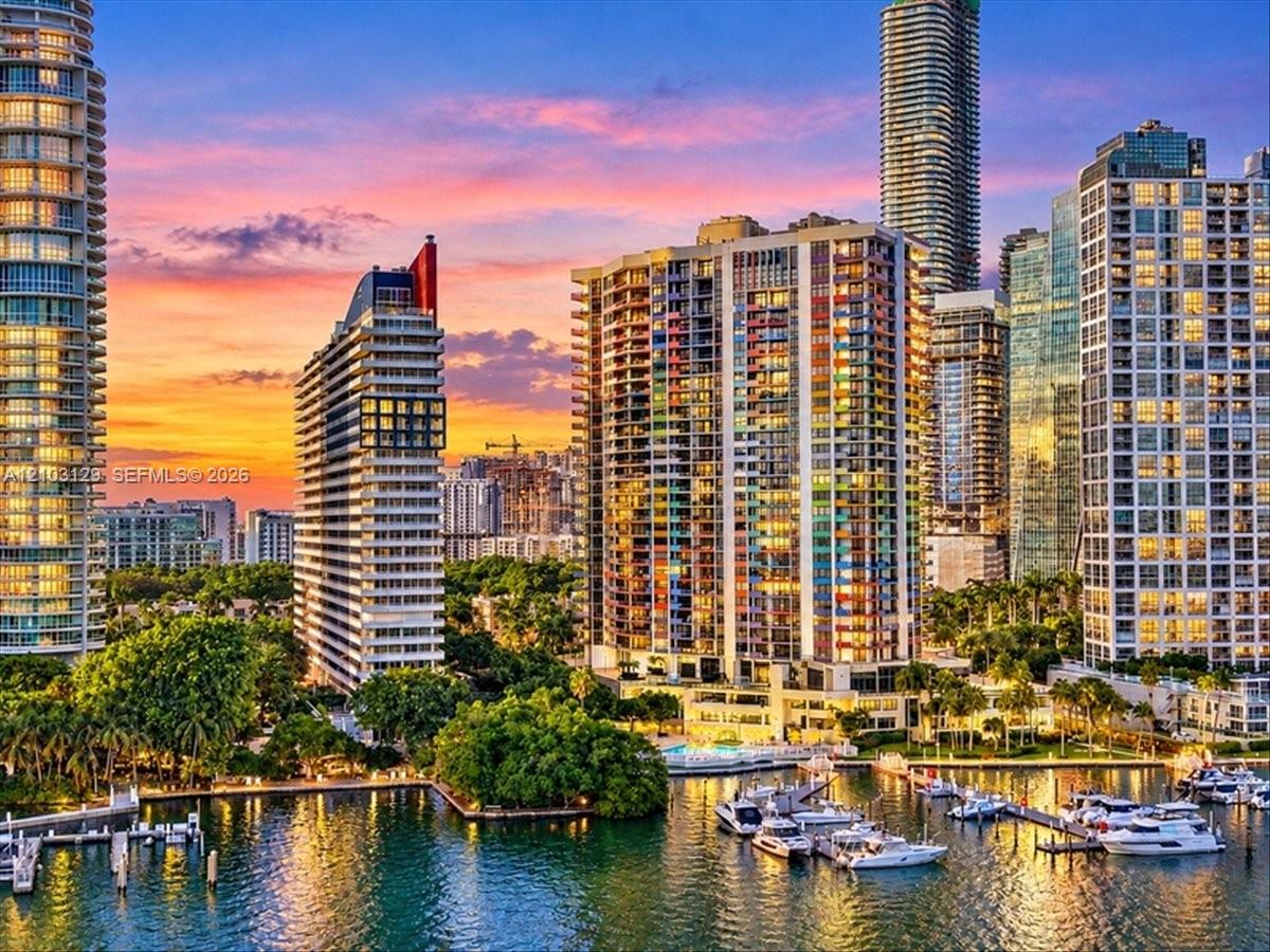 High-rise urban landscape featuring multiple glass-facade residential towers, deep-water marina with boat slips, and mature tropical landscaping set against a coastal waterway