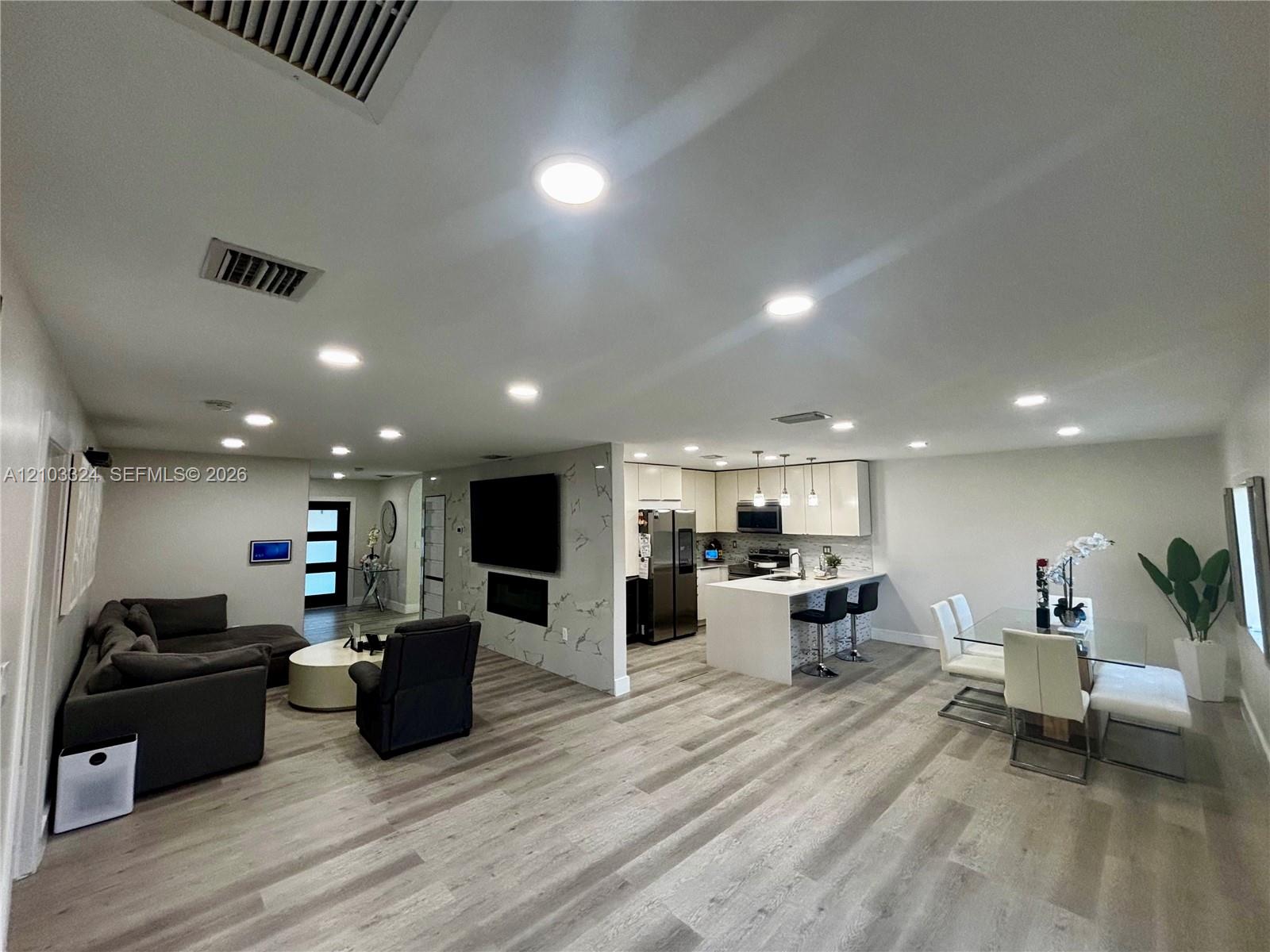 Open-concept interior featuring wood-finish flooring, recessed lighting, a stone-finish accent wall with an integrated fireplace, and a kitchen island with stone-finish countertops Open-concept interior featuring wood-finish flooring, recessed lighting, a stone-finish accent wall with an integrated fireplace, and a kitchen island with stone-finish countertops