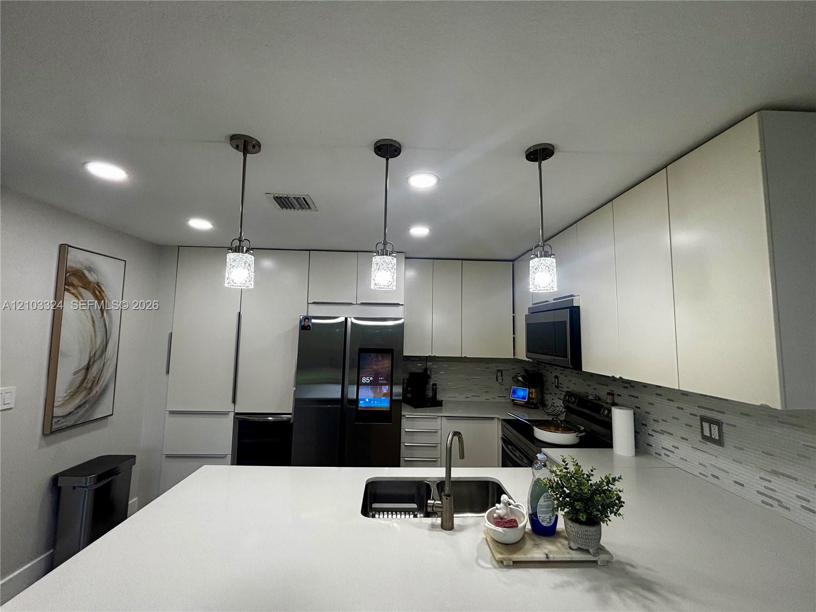 Kitchen featuring slab countertops, flat-panel cabinetry, recessed lighting, glass pendant fixtures, and a dual-basin undermount sink with a gooseneck faucet Kitchen featuring slab countertops, flat-panel cabinetry, recessed lighting, glass pendant fixtures, and a dual-basin undermount sink with a gooseneck faucet