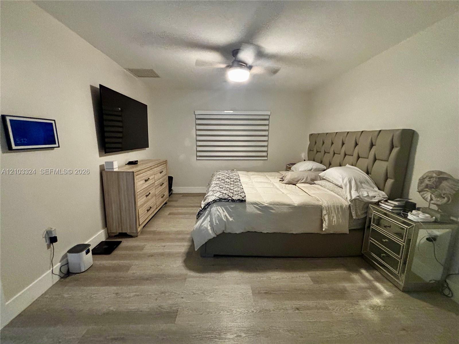 Neutral-toned interior featuring wood-finish flooring, a ceiling fan with integrated lighting, and horizontal window blinds