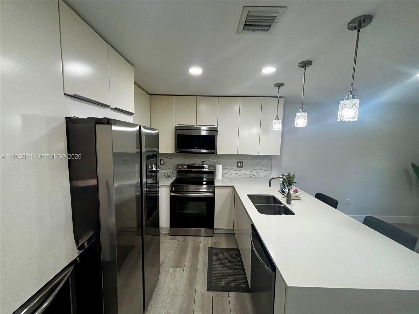 Kitchen featuring flat-panel cabinetry, quartz countertops, a double-basin stainless steel sink with a pull-down faucet, stainless steel appliances, and wood-finish flooring Kitchen featuring flat-panel cabinetry, quartz countertops, a double-basin stainless steel sink with a pull-down faucet, stainless steel appliances, and wood-finish flooring