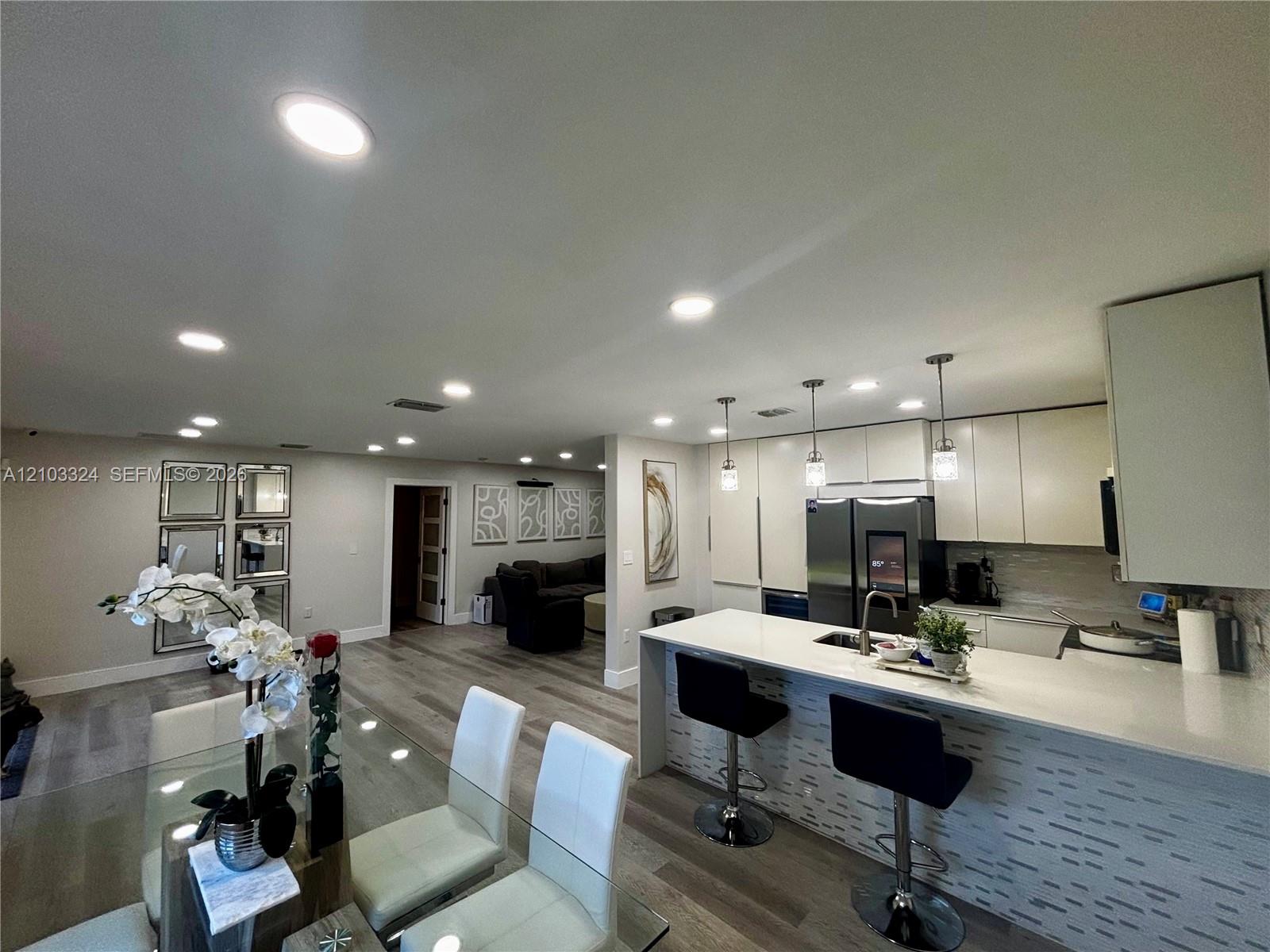Kitchen featuring flat-panel cabinetry, quartz countertops, a waterfall island, recessed lighting, and pendant fixtures over the breakfast bar Kitchen featuring flat-panel cabinetry, quartz countertops, a waterfall island, recessed lighting, and pendant fixtures over the breakfast bar