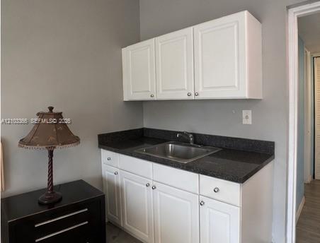 White cabinetry featuring shaker-style doors, dark stone-finish countertop, and stainless steel undermount sink