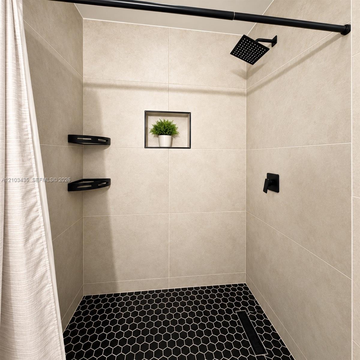 Shower stall featuring large-format beige wall tile, hexagonal black floor tile, matte black rainfall shower head, integrated wall niche, and corner shelving Shower stall featuring large-format beige wall tile, hexagonal black floor tile, matte black rainfall shower head, integrated wall niche, and corner shelving