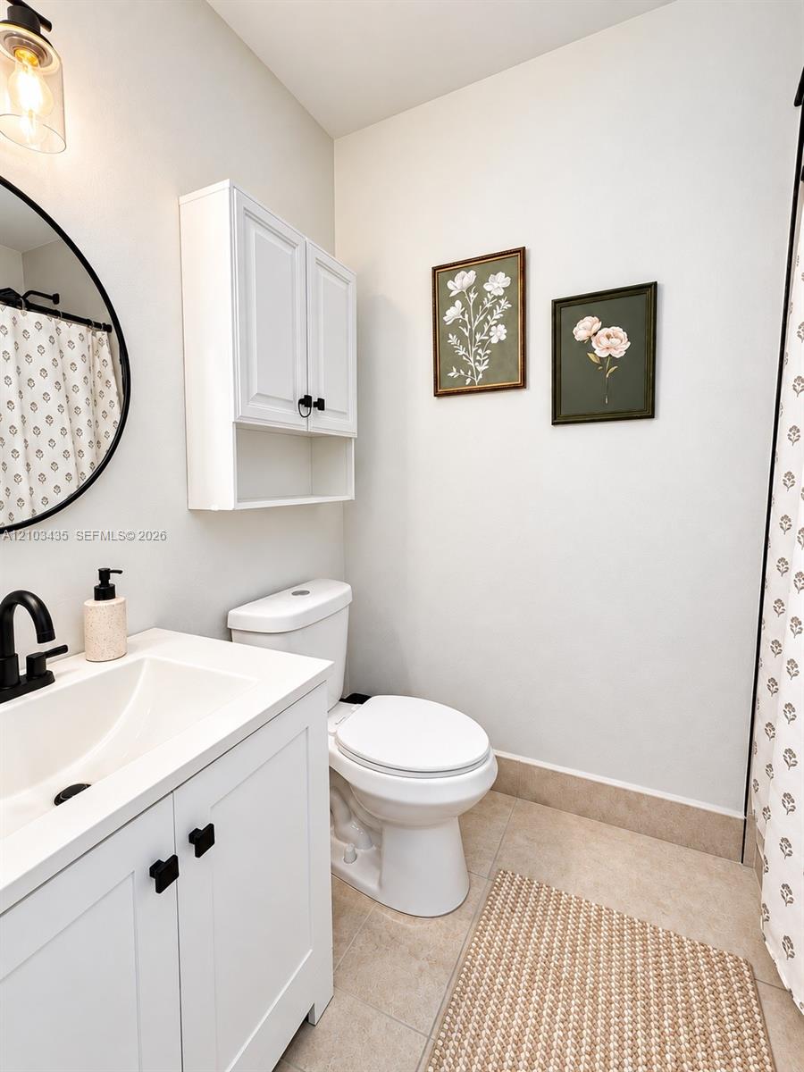 White vanity with a rectangular sink, matte black faucet, wall-mounted storage cabinet, circular mirror, and tile flooring White vanity with a rectangular sink, matte black faucet, wall-mounted storage cabinet, circular mirror, and tile flooring