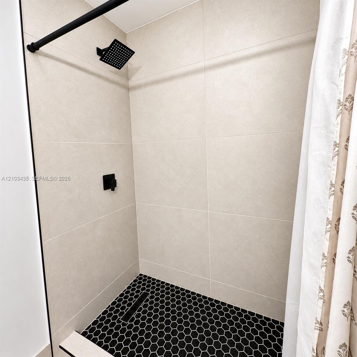 Shower featuring large-format neutral wall tile, black hexagon floor tile, matte black rain-style shower head, and matte black single-handle mixing valve