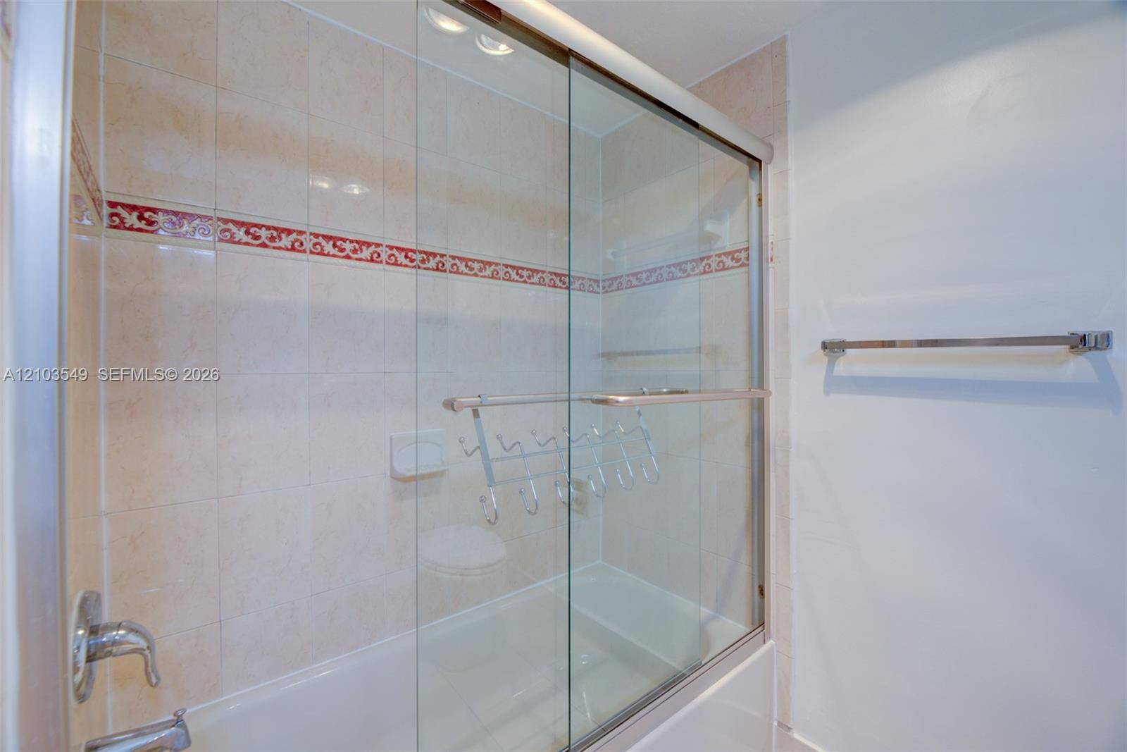 Shower-tub combination featuring sliding glass doors, neutral ceramic wall tile, a decorative red accent tile border, and metallic hardware