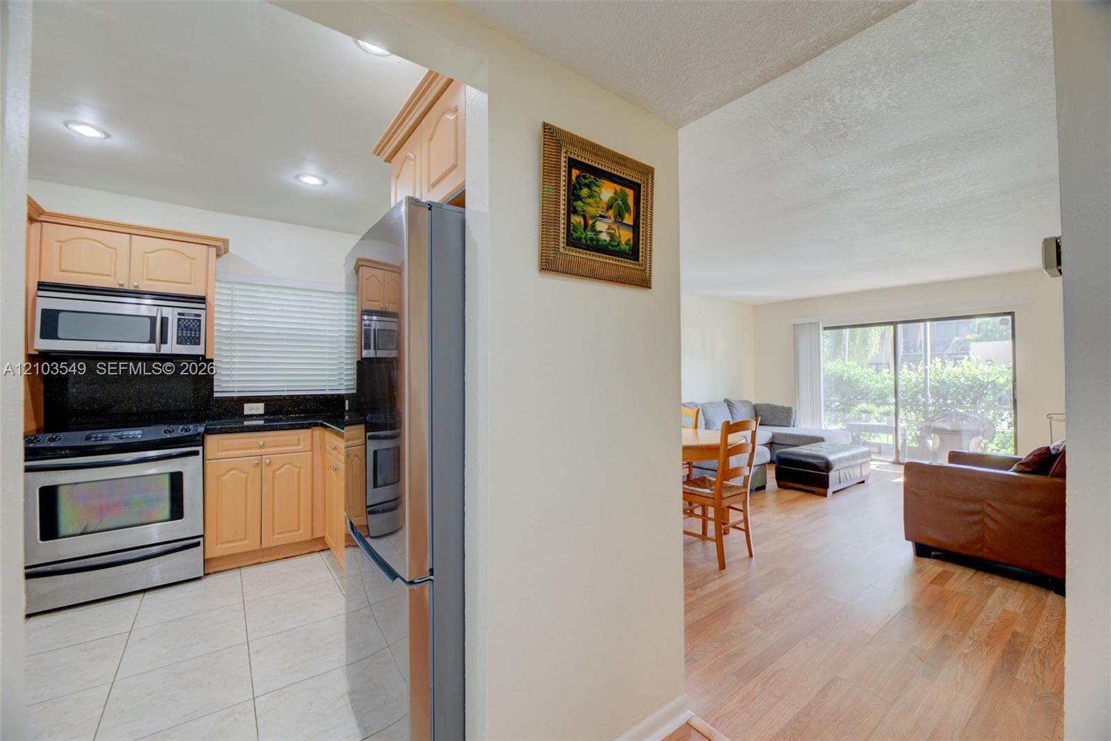Kitchen featuring light-finish cabinetry, dark solid-surface countertops, and stainless steel appliances, complemented by wood-finish flooring and recessed lighting Kitchen featuring light-finish cabinetry, dark solid-surface countertops, and stainless steel appliances, complemented by wood-finish flooring and recessed lighting