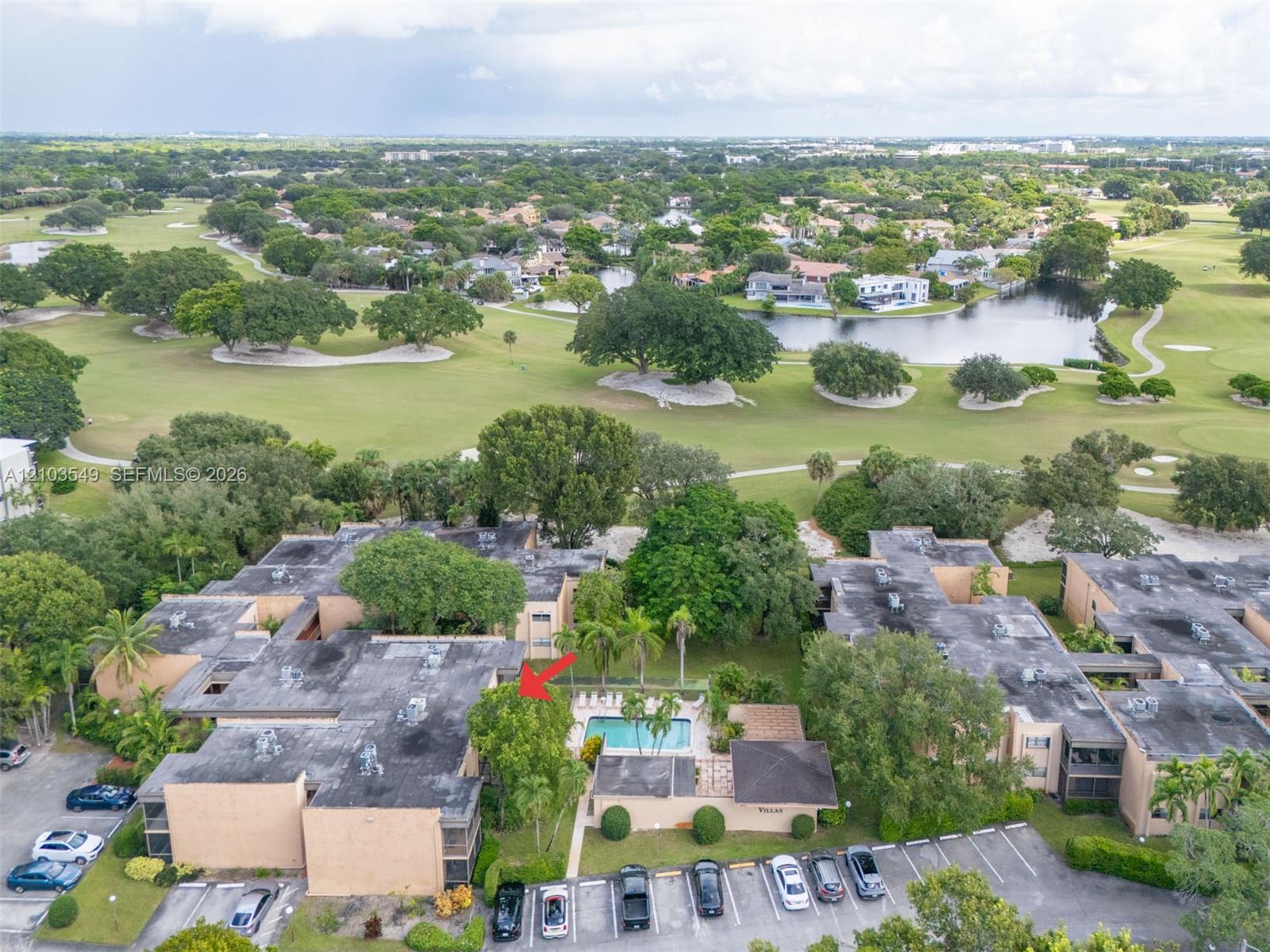 Aerial perspective of multi-family property featuring an outdoor swimming pool, paved parking area, and proximity to golf course grounds and water features