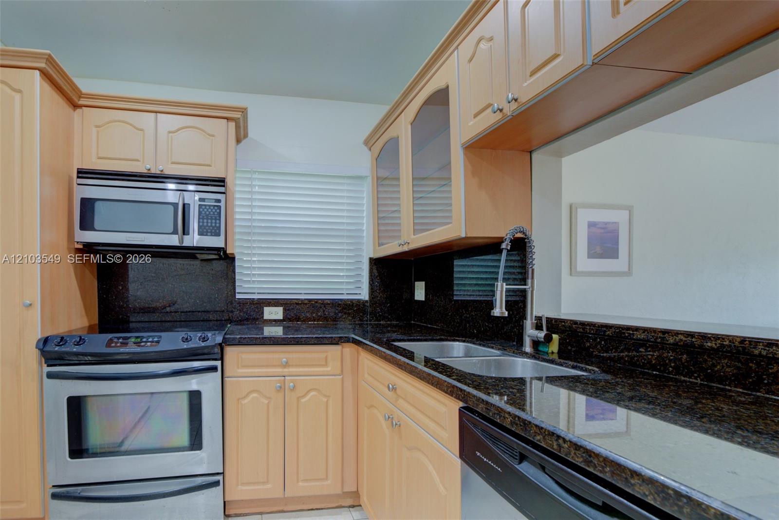 Kitchen featuring light-tone cabinetry, dark stone countertops, stainless steel appliances, dual-basin stainless steel sink with high-arc pull-down faucet, and glass-panel upper cabinet doors
