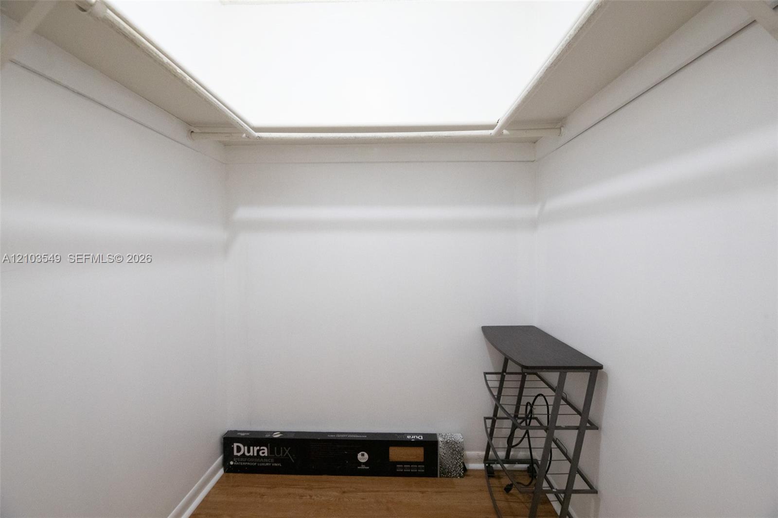 Reach-in storage closet featuring wood-finish flooring, white walls, overhead lighting, and white built-in shelving rods