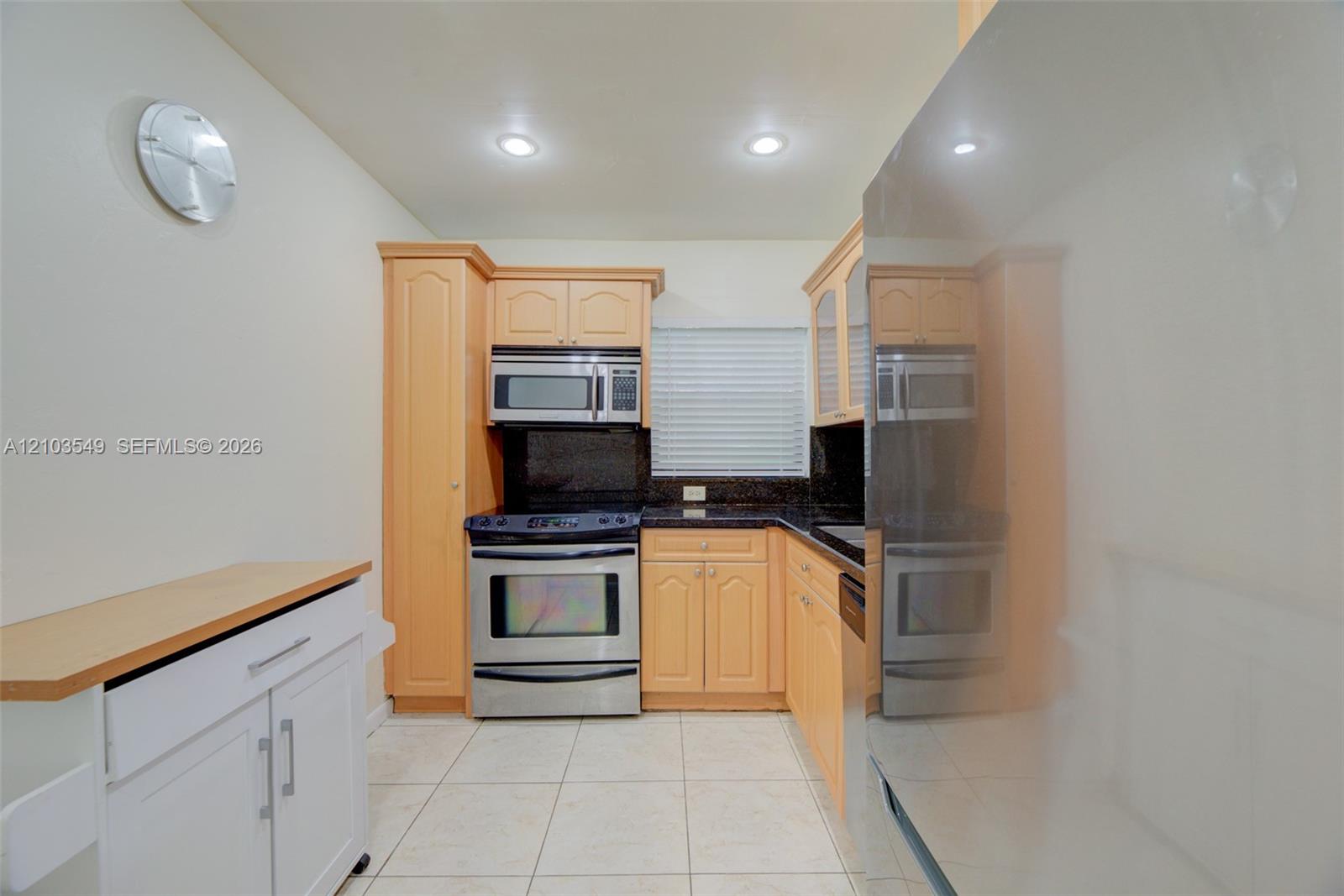 Kitchen featuring light wood cabinetry, dark stone countertops, stainless steel appliances, tile flooring, and recessed ceiling lighting