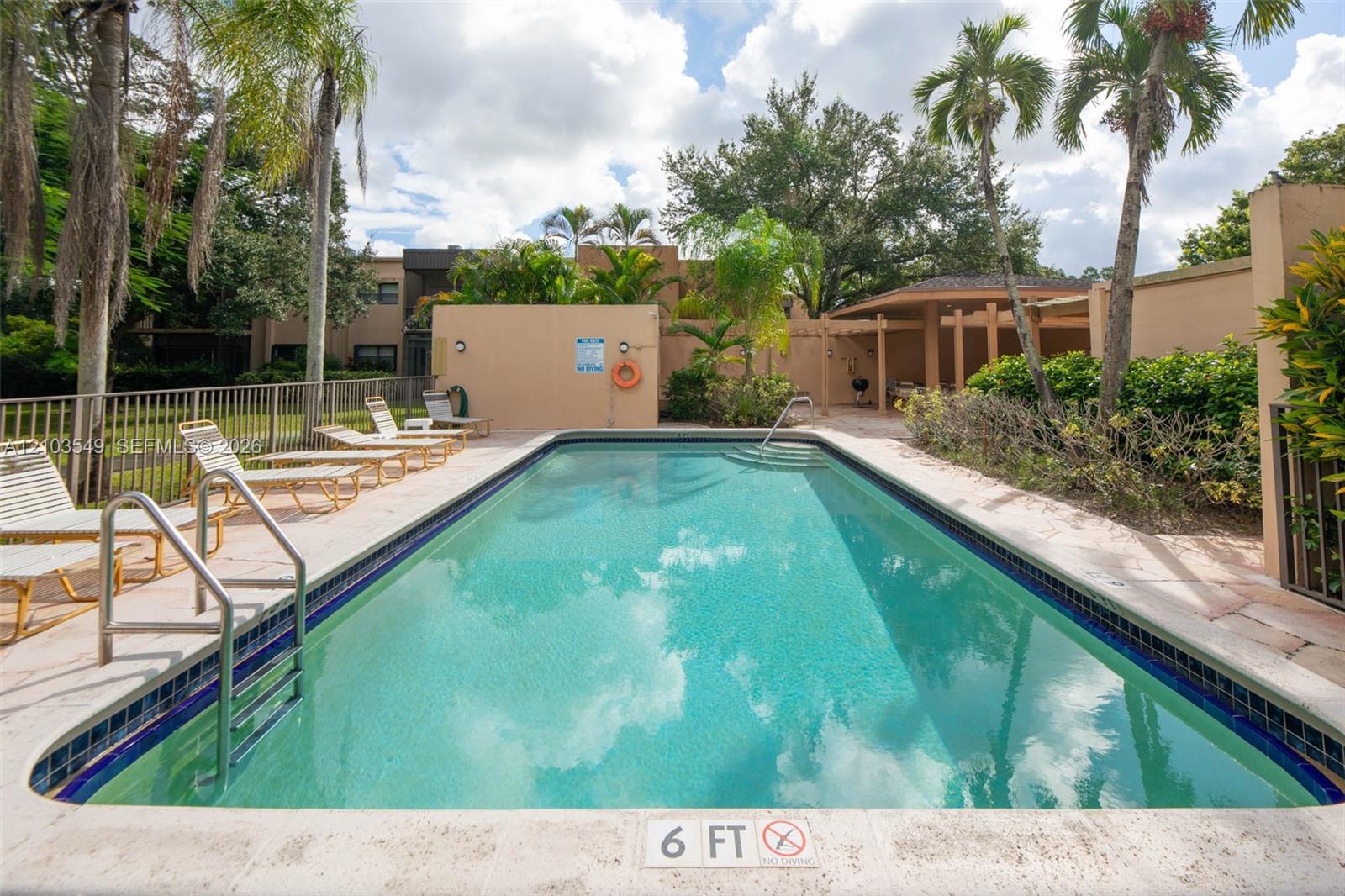 In-ground swimming pool featuring a tiled waterline, stone-finish pool deck, metal handrail, and covered pergola