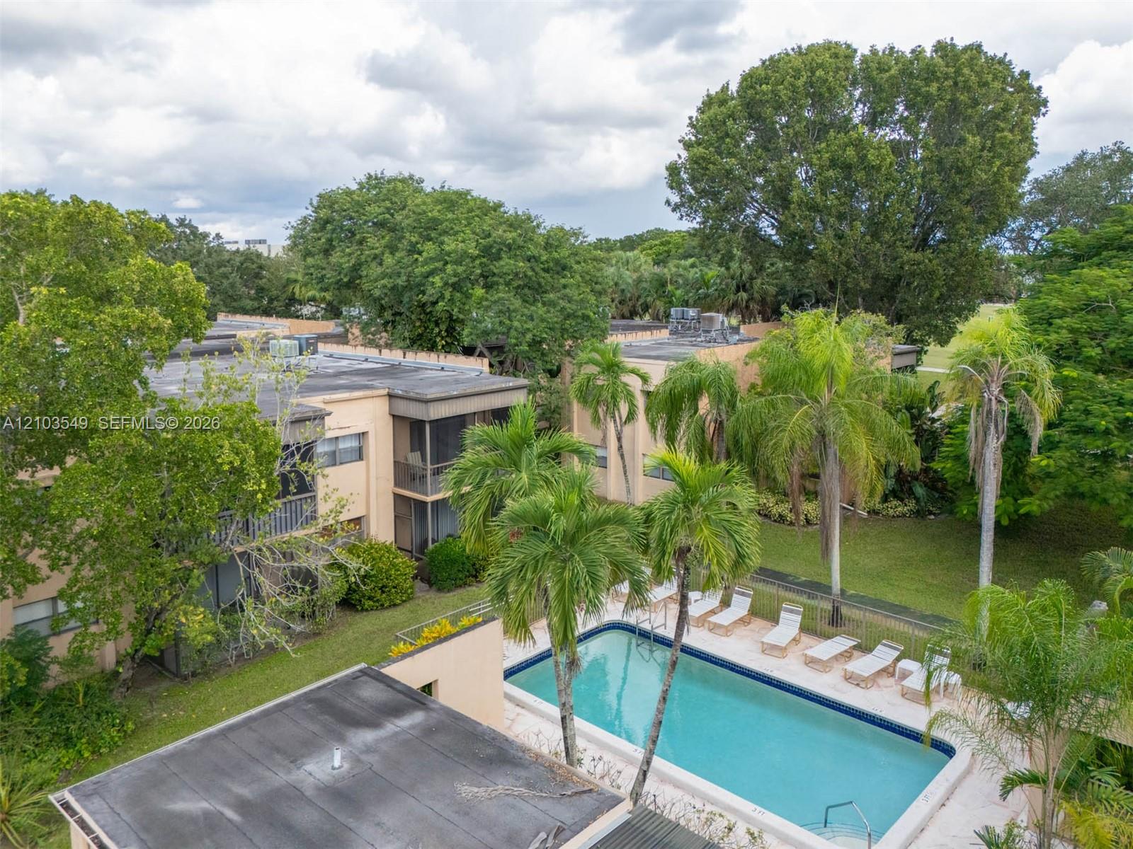 Multi-story residential building with screened lanais and stucco exterior, featuring a swimming pool, concrete pool deck, and mature palms