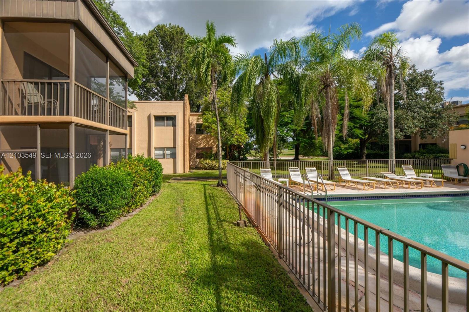 Multi-level screened lanais featuring exterior railings, swimming pool enclosed by metal fencing, and manicured landscaping with mature palm trees