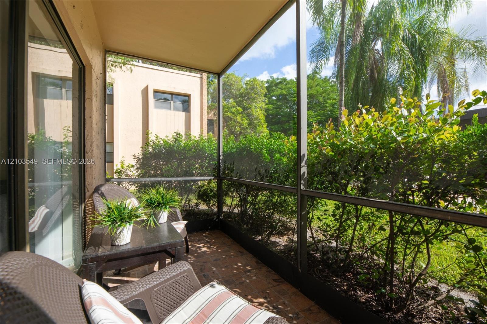 Screened-in lanai featuring brick pavers and exterior access to surrounding mature landscaping