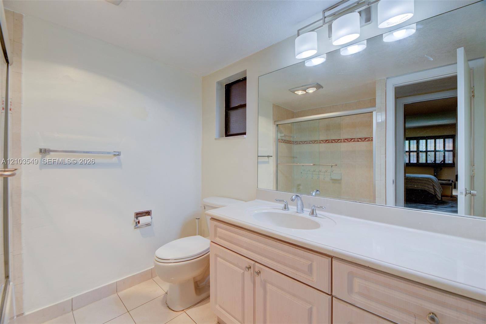 Bathroom featuring a vanity with integrated sink and countertop, full-width wall mirror, four-light vanity fixture, and a glass-enclosed shower