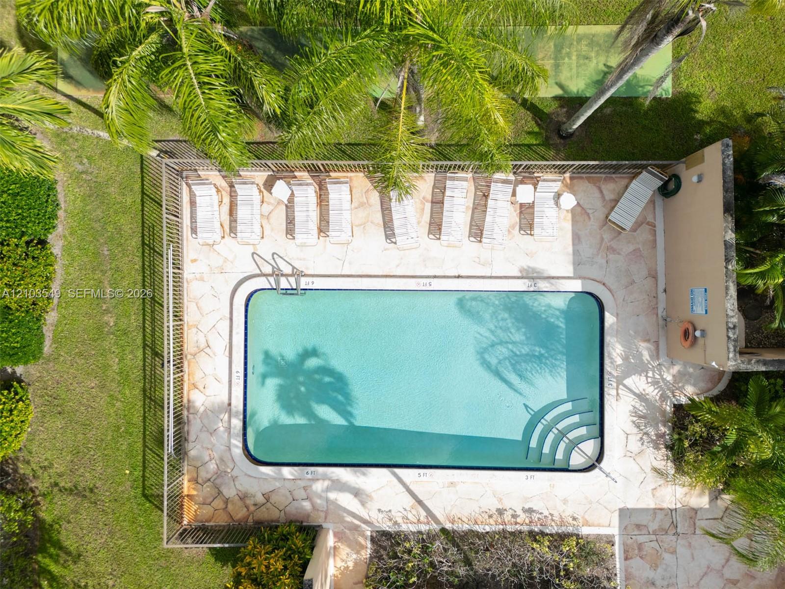 In-ground pool featuring built-in stairs, perimeter fencing, flagstone patio, and mature palm trees