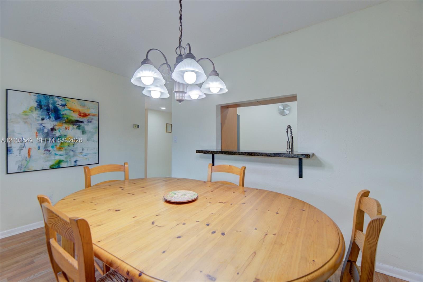 Dining space featuring a multi-bulb chandelier and a wall pass-through with a stone-finish ledge
