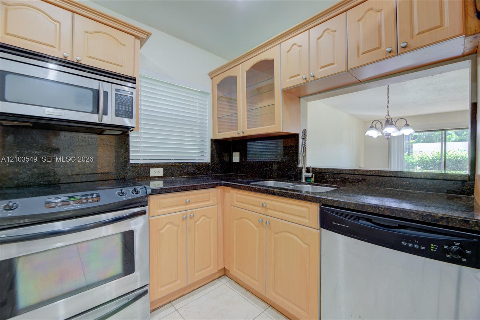 Kitchen featuring light-finish cabinetry with glass-front uppers, dark stone-surround countertops, a stainless steel over-the-range microwave, stainless steel range, and a pass-through window