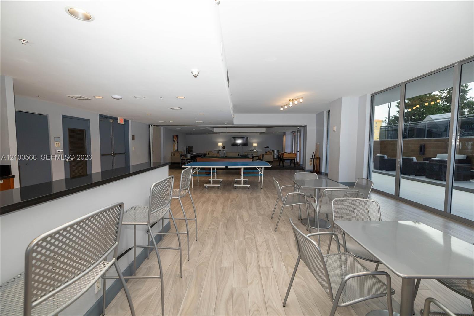 Open-concept common area featuring wood-finish flooring, a built-in refreshment bar with a stone countertop, recessed lighting, and expansive floor-to-ceiling glass sliding doors