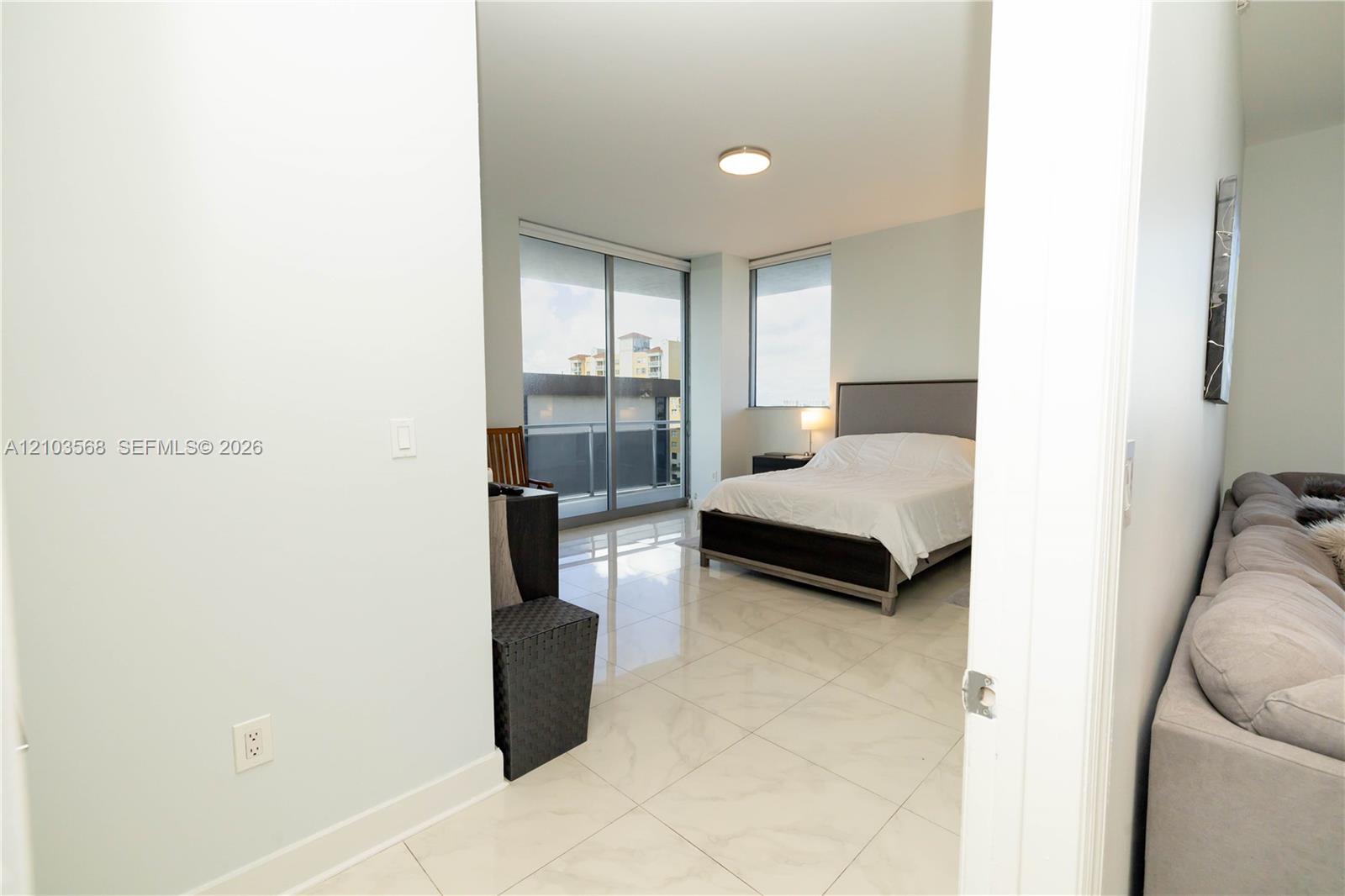 Polished stone-finish tile flooring, floor-to-ceiling glass sliding door, balcony access, and large-format windows with integrated roller shades