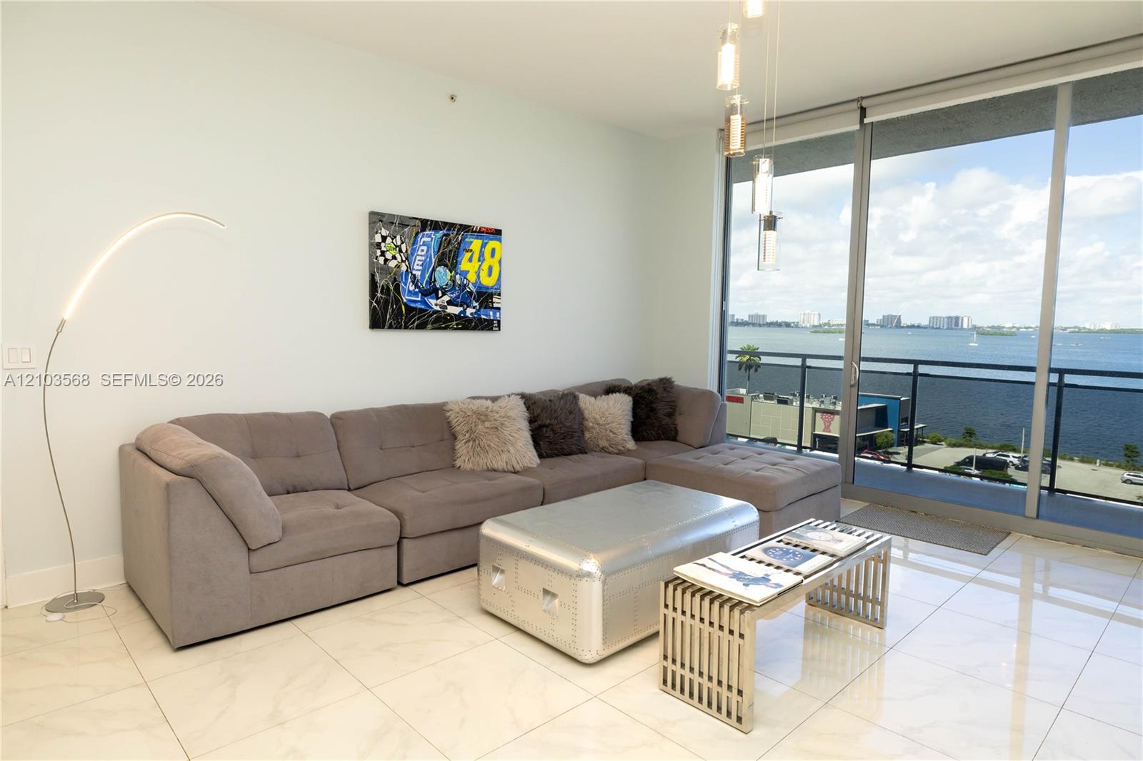 Floor-to-ceiling glass sliding doors, polished tile flooring, balcony with metal railing, and multi-pendant contemporary light fixture