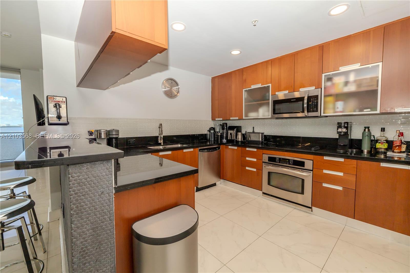 Kitchen featuring wood cabinetry, black countertops, stainless steel appliances, tiled flooring, and a peninsula breakfast bar
