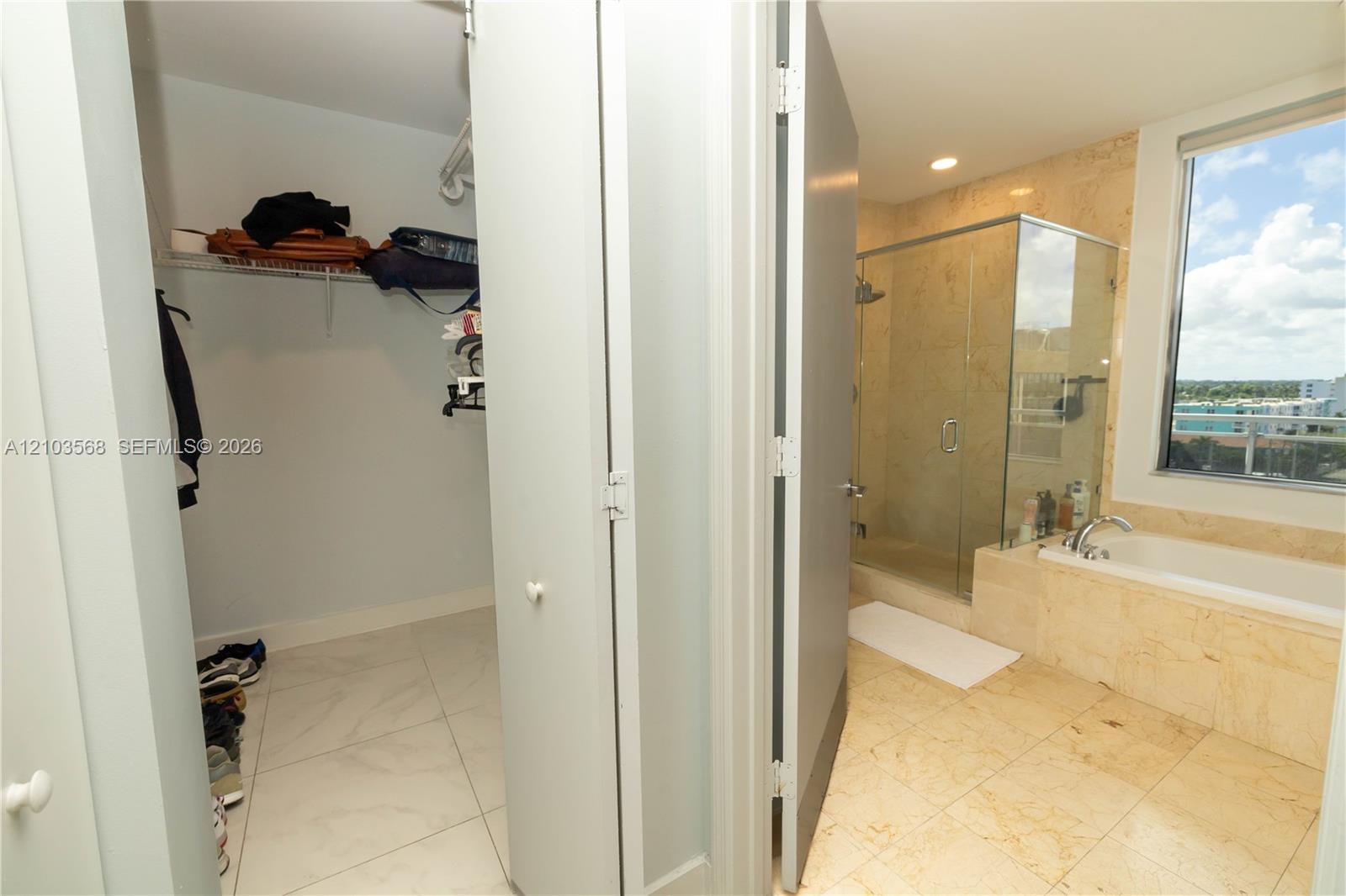 Bathroom featuring a glass-enclosed shower, stone-surround soaking tub, stone tile flooring, and a walk-in closet with built-in shelving