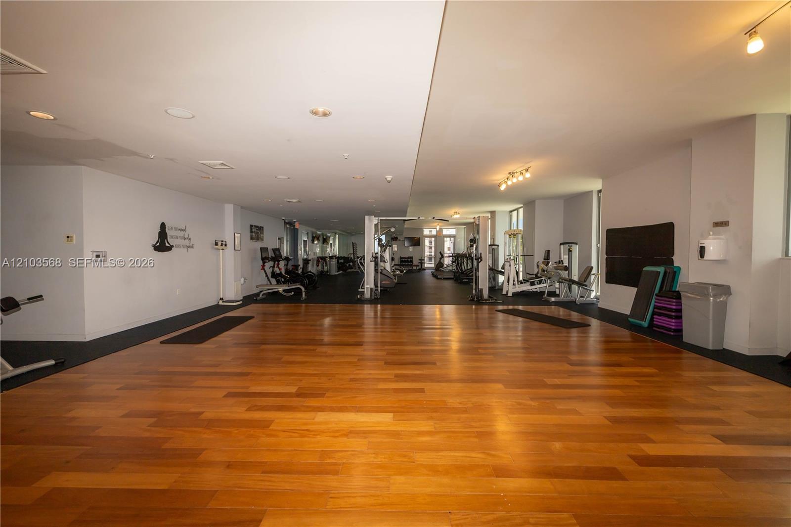 Spacious fitness area featuring wood-finish flooring, recessed ceiling lighting, and track lighting fixtures
