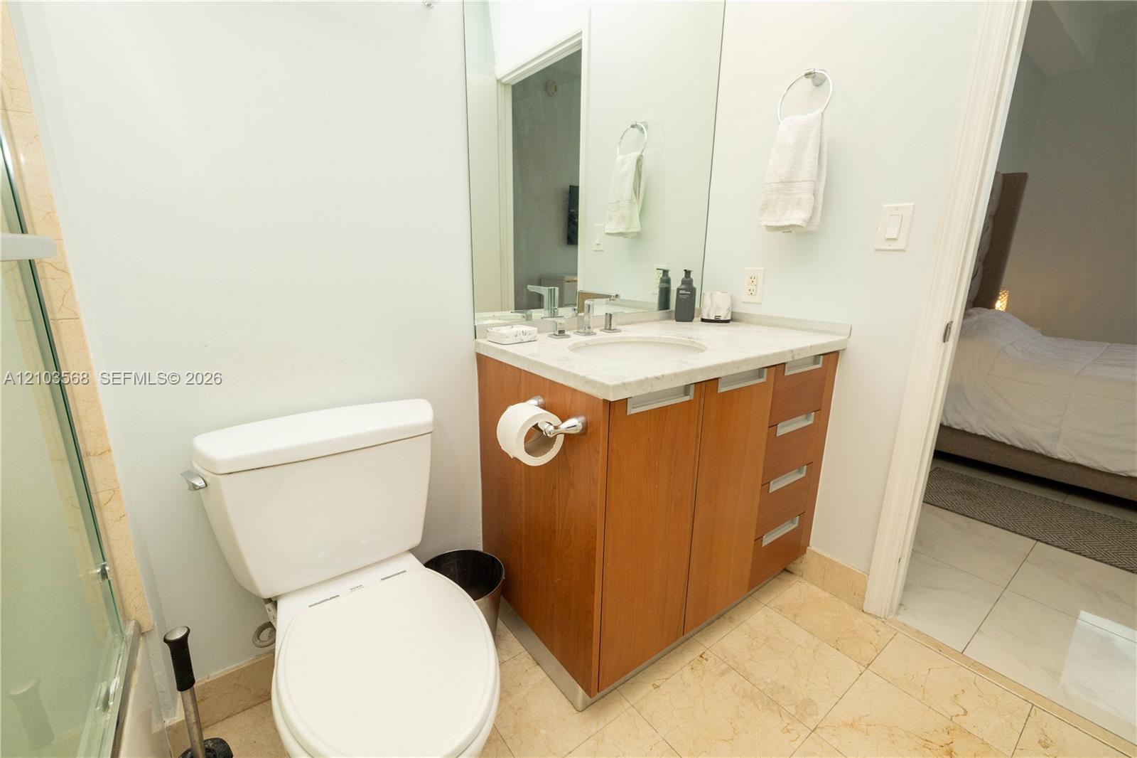 Wood-finish vanity with a stone countertop, integrated sink, large wall-mounted mirror, and tile flooring