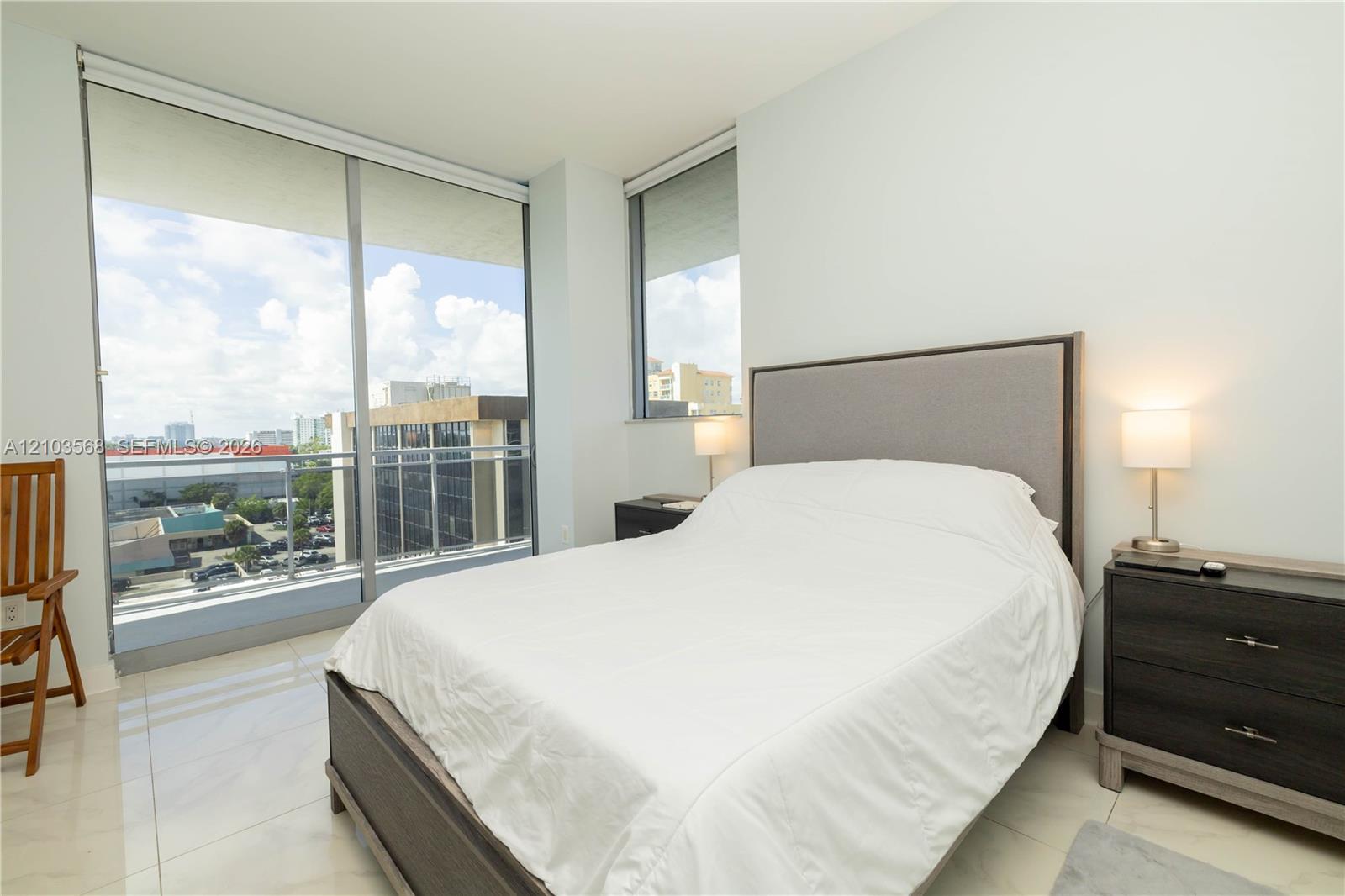 Floor-to-ceiling windows, private balcony with metal railing, and light-toned tile flooring