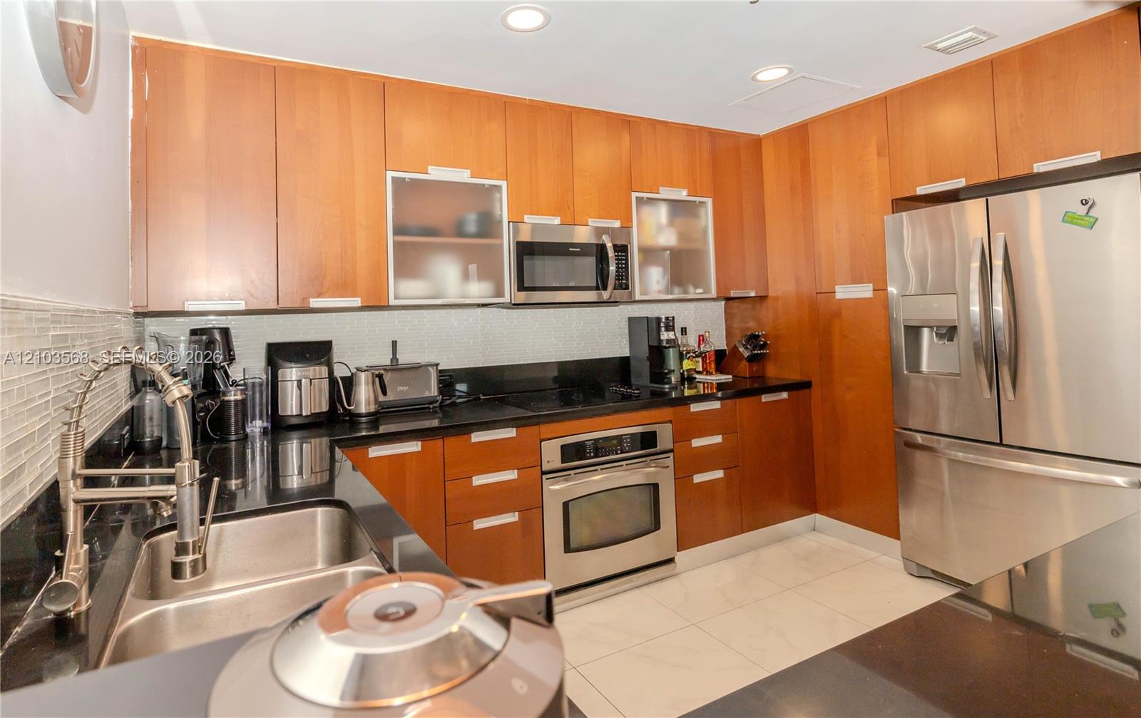 Kitchen featuring full-height wood cabinetry, dark stone countertops, stainless steel appliances, a mosaic tile backsplash, and recessed lighting