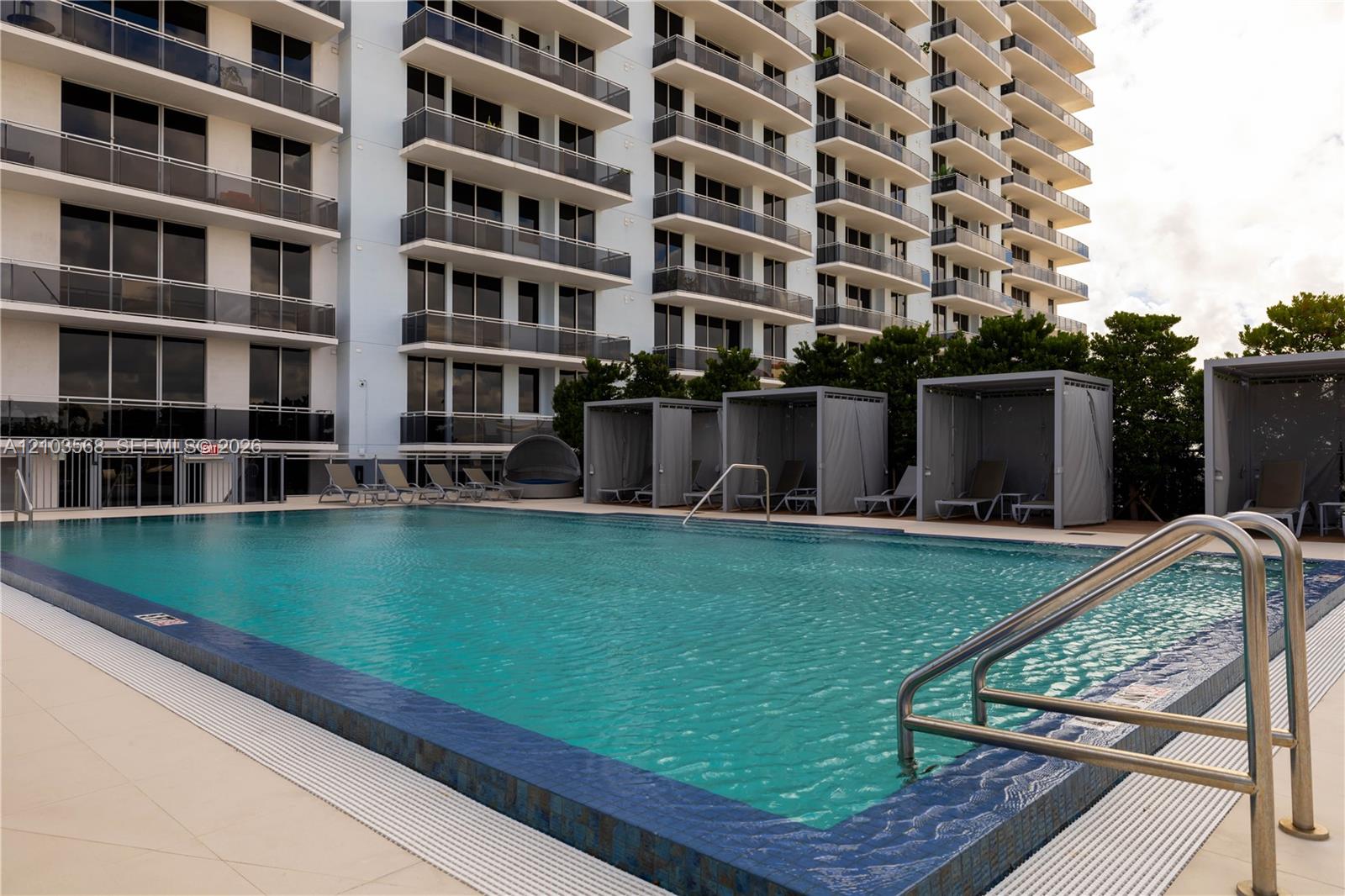 Swimming pool featuring tiled coping, metal handrails, and a surrounding paved deck