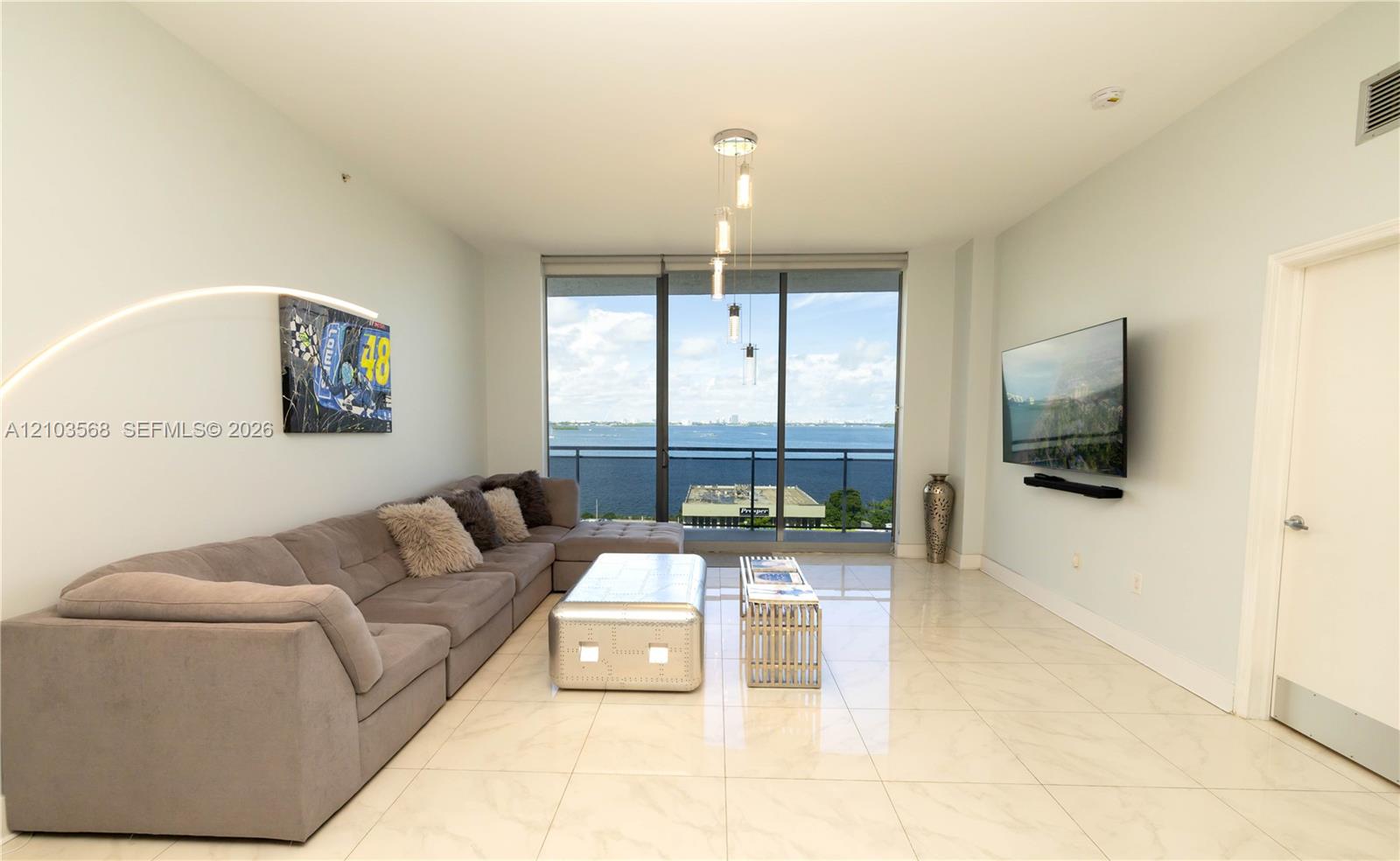Living area featuring large-format tile flooring, floor-to-ceiling glass windows, a private balcony, and pendant lighting