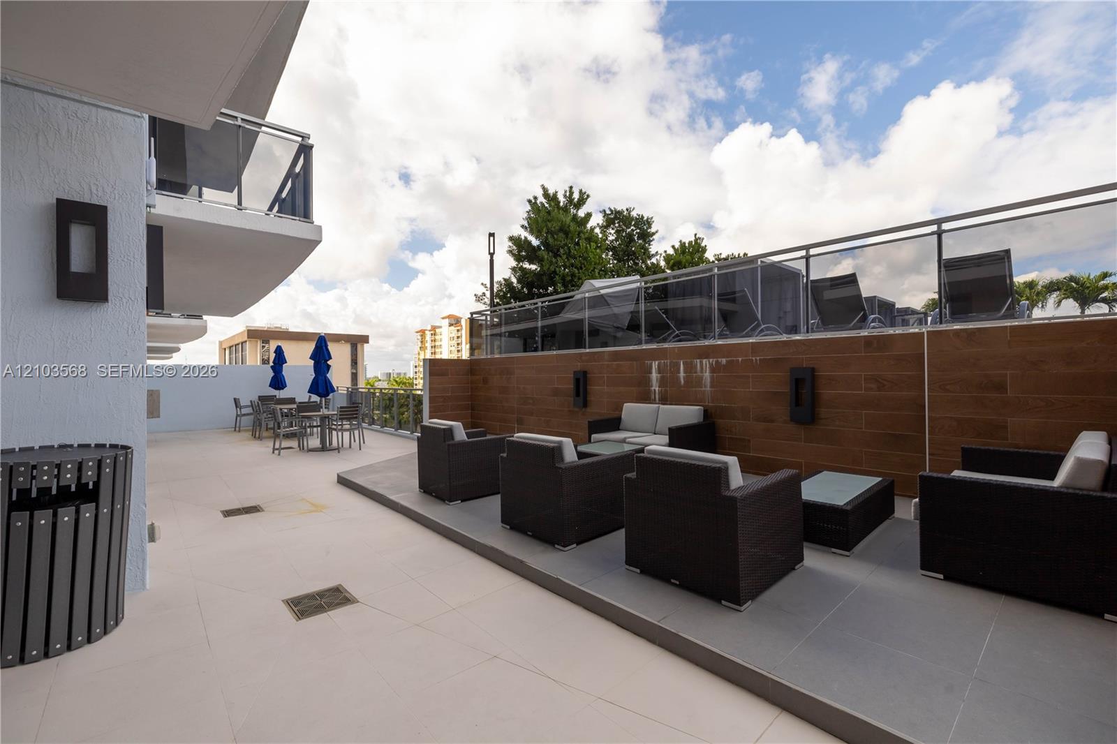 Expansive outdoor terrace featuring large-format tile flooring, wood-finish wall cladding, glass-panel railings, and integrated wall-mounted lighting