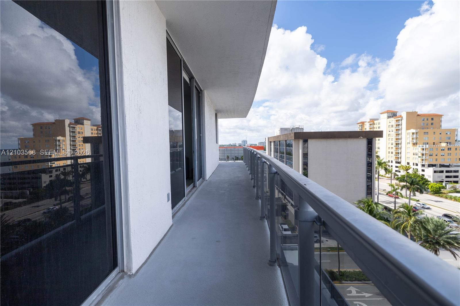 Covered balcony featuring concrete flooring, full-length glass sliding doors, and a metal railing with glass panels