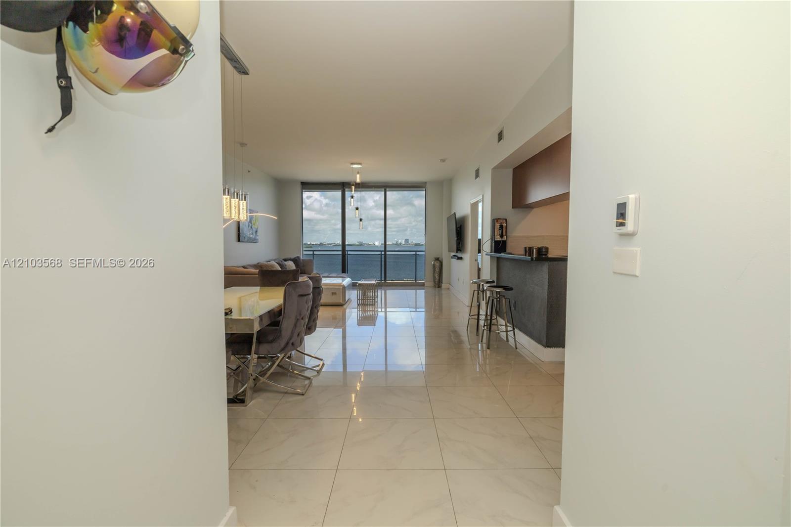 Open-concept interior featuring large-format tile flooring, kitchen breakfast bar with integrated cabinetry, and floor-to-ceiling glass wall