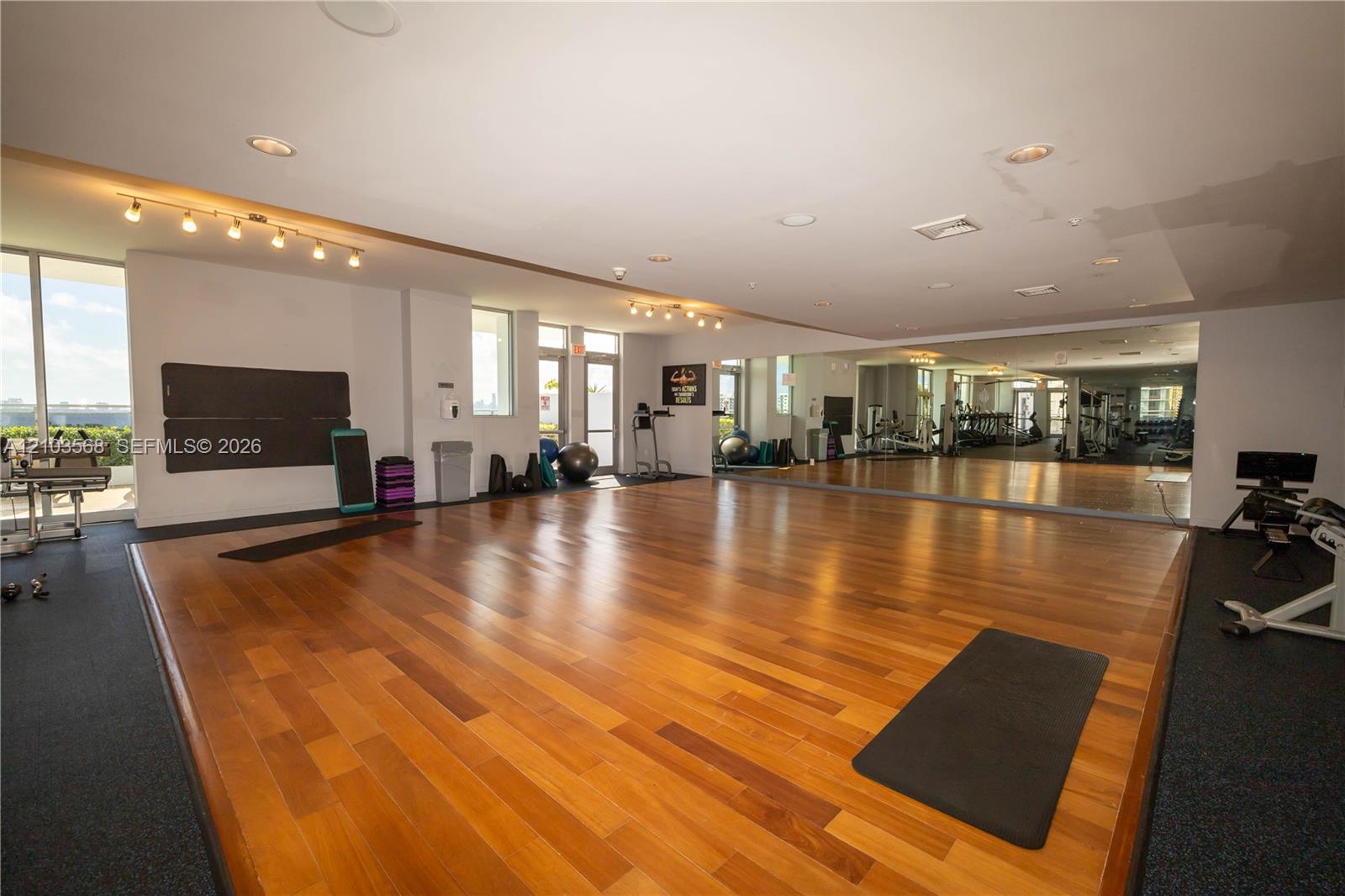 Fitness center featuring wood-finish flooring, full-length wall mirrors, recessed lighting, track lighting, and floor-to-ceiling glass doors