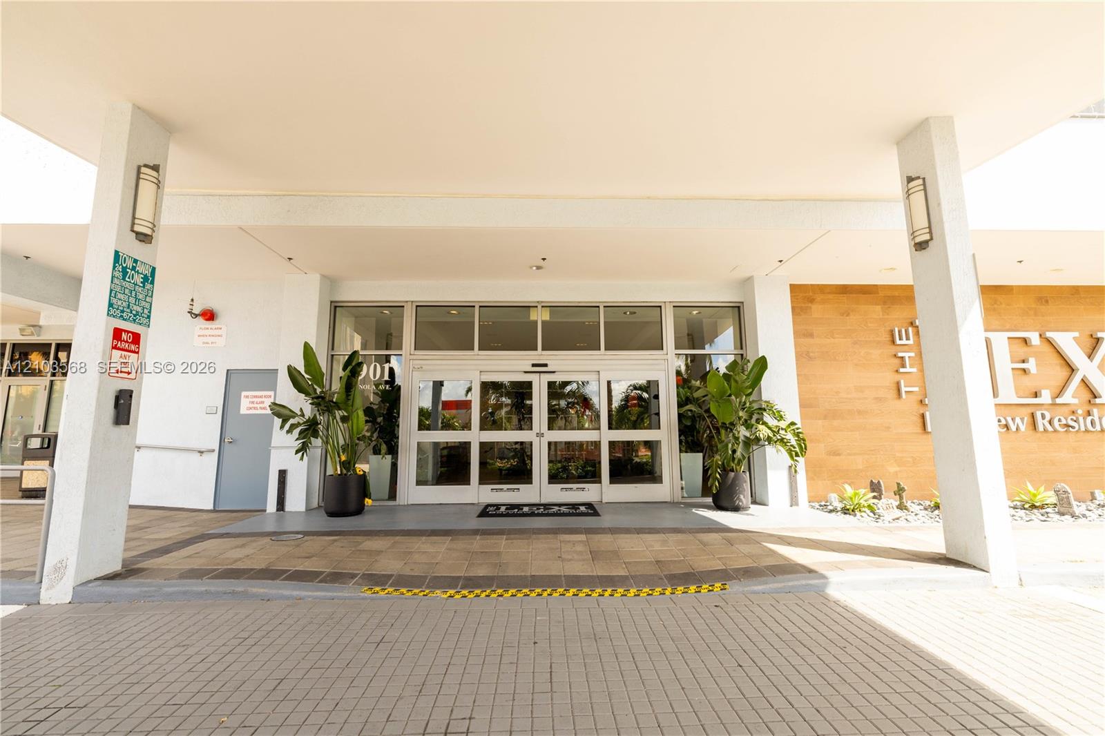 Covered building entrance featuring a stone-paved driveway, multi-pane glass sliding doors, wall-mounted exterior sconces, and wood-finish paneling