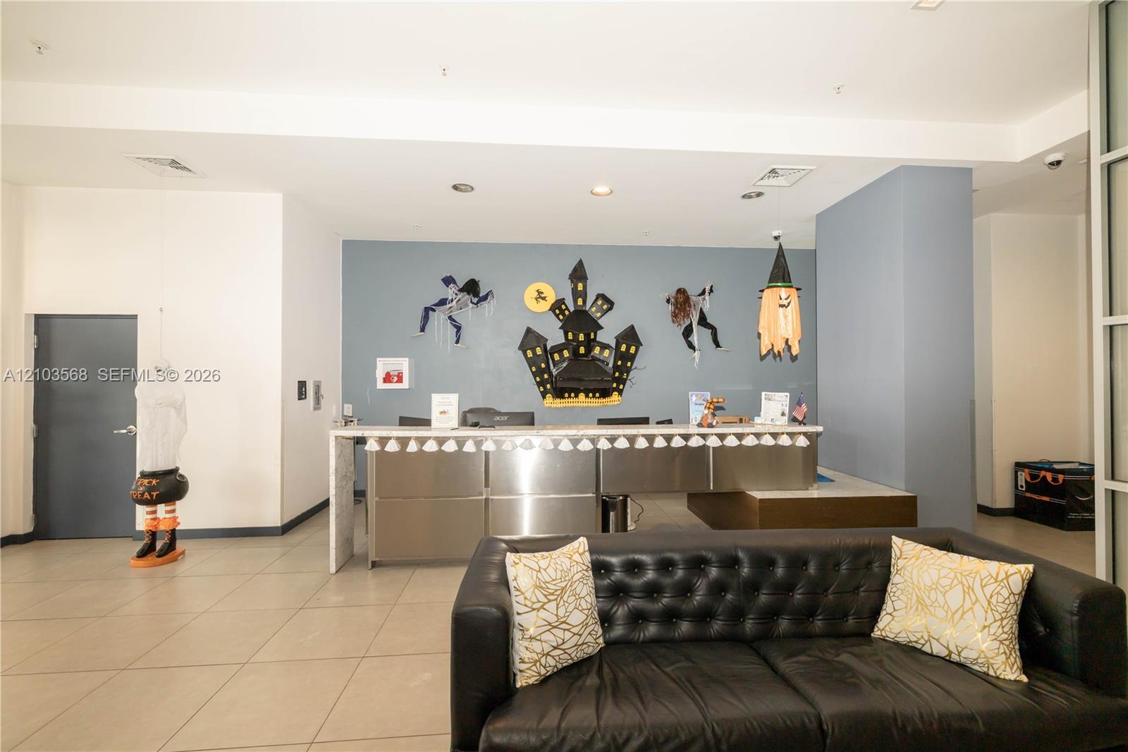Reception area featuring high ceilings, neutral tile flooring, recessed lighting, and a built-in stainless steel desk with a stone-finish countertop