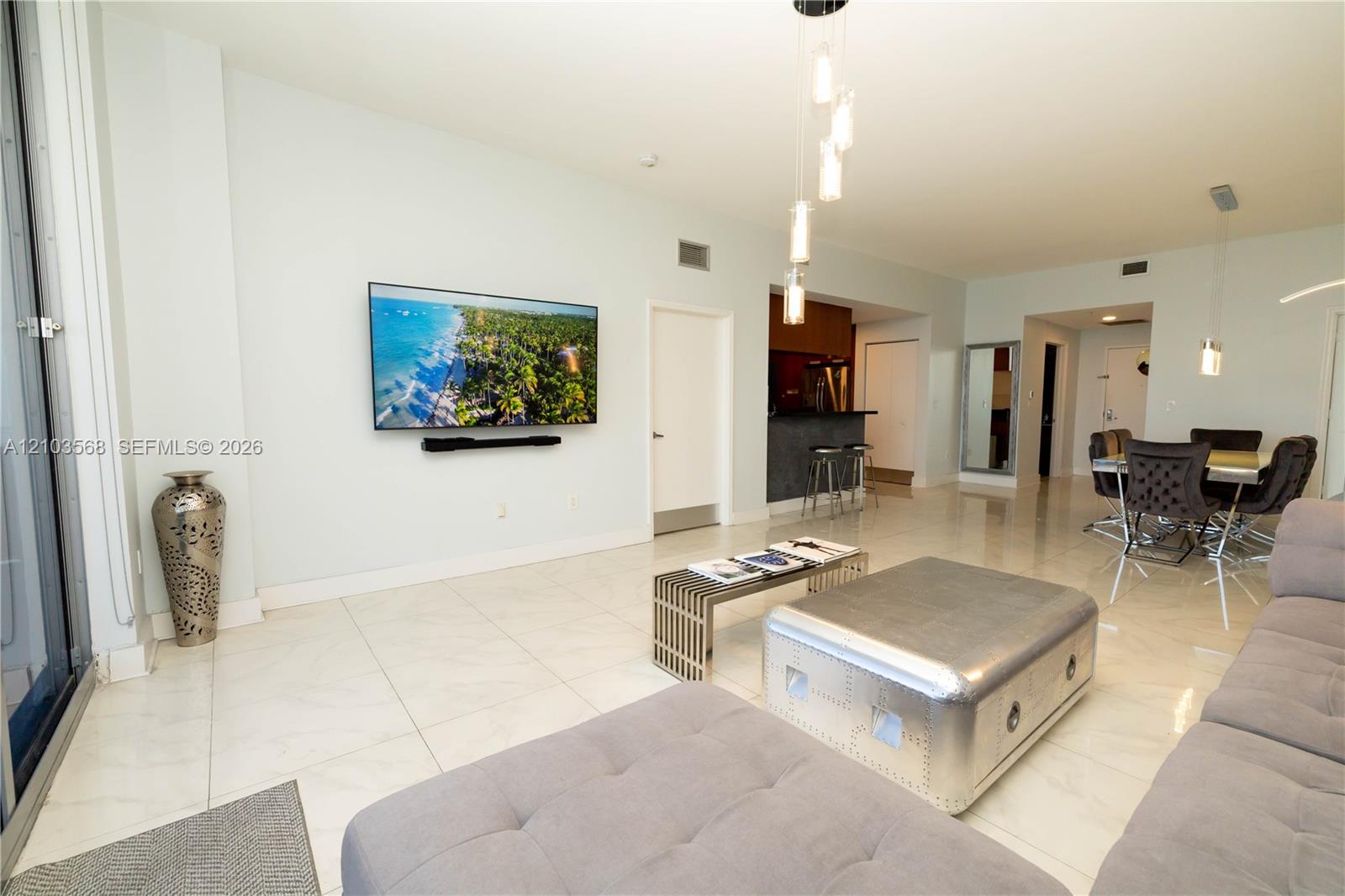 Open-concept living space featuring large-format tile flooring, multi-pendant overhead lighting, and a kitchen area with a built-in counter