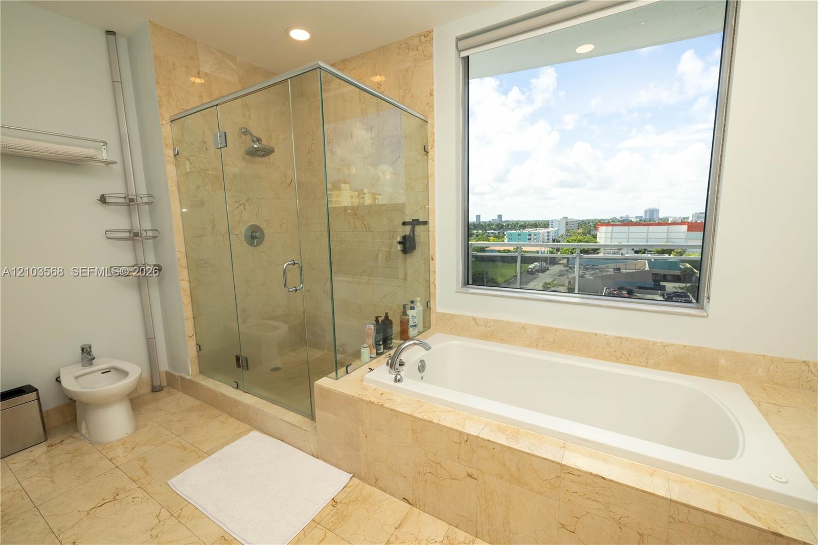 Bathroom featuring stone-finish flooring and wall tiling, a glass-enclosed shower, a drop-in soaking tub, and a bidet
