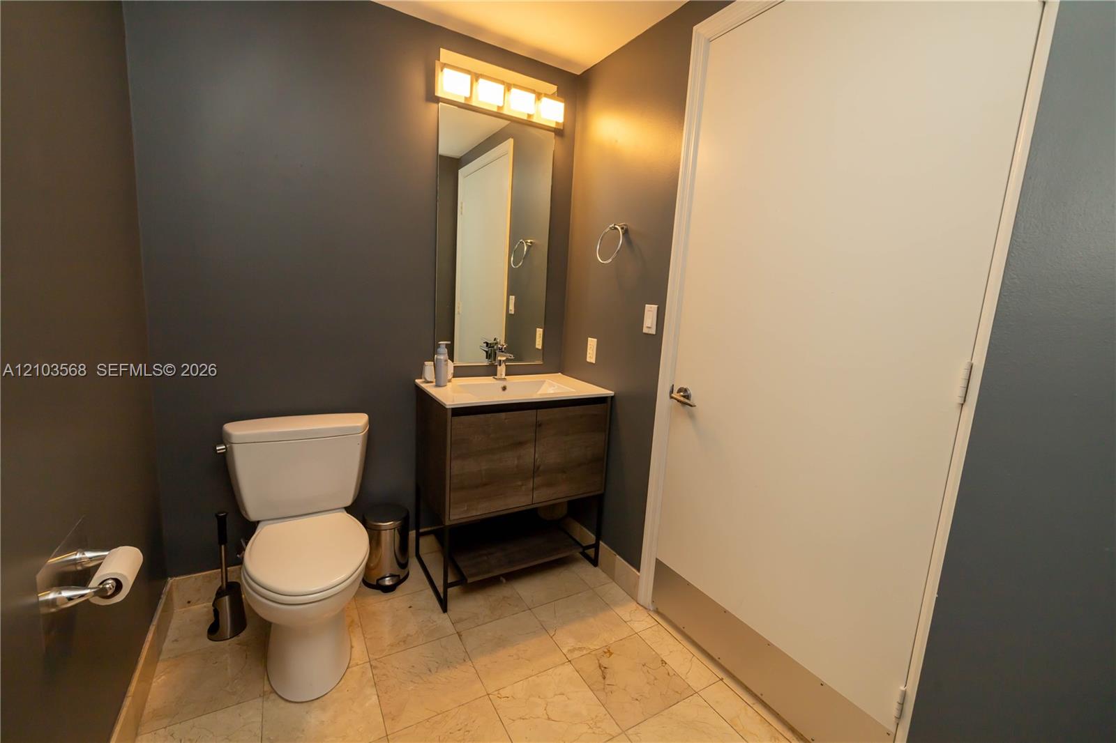 Bathroom featuring a wood-finish vanity with a rectangular sink, integrated light fixture above a rectangular mirror, and stone-finish flooring