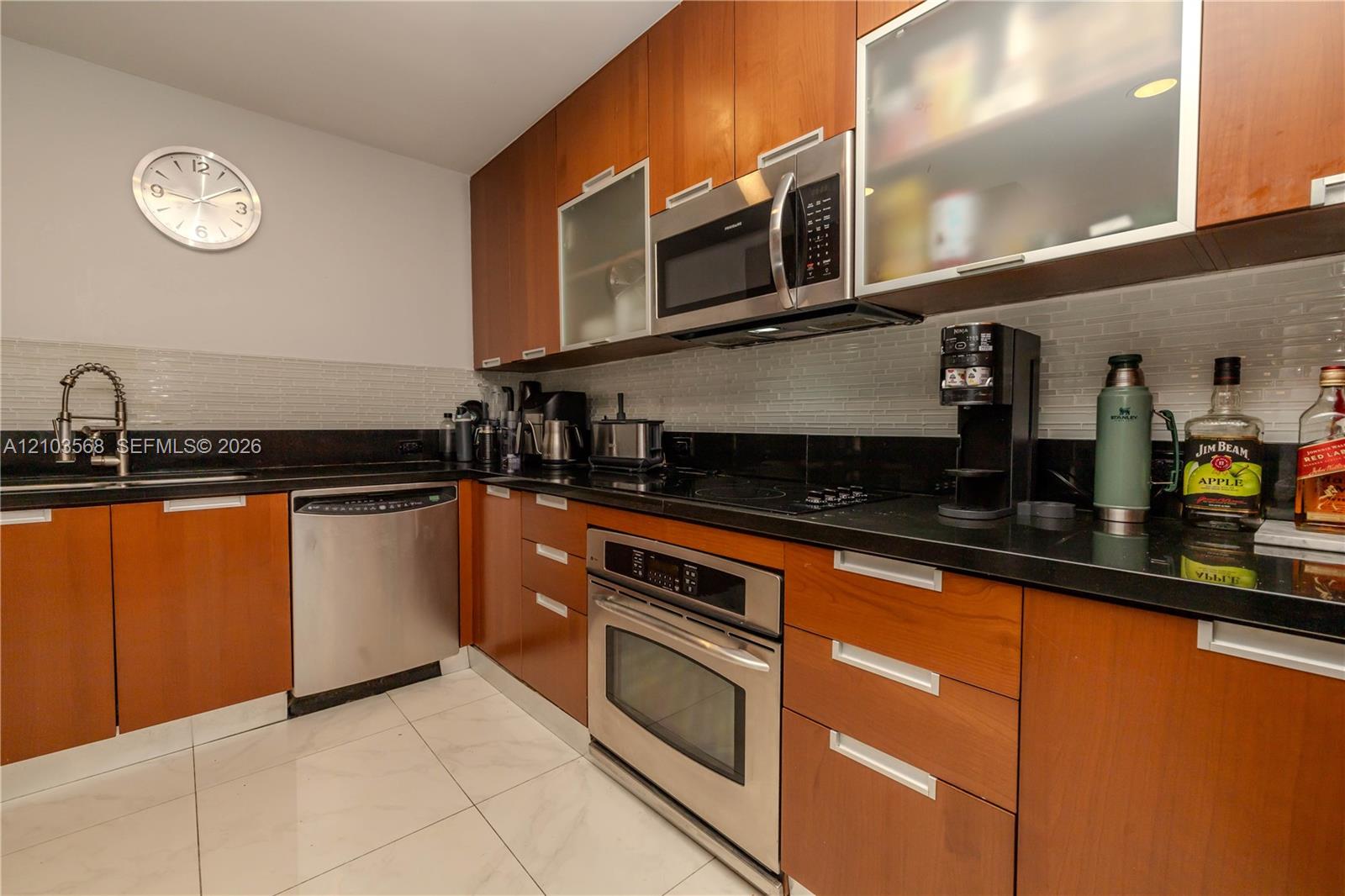 Kitchen featuring flat-panel wood cabinetry, black countertops, stainless steel appliances, tiled backsplash, and light-toned flooring