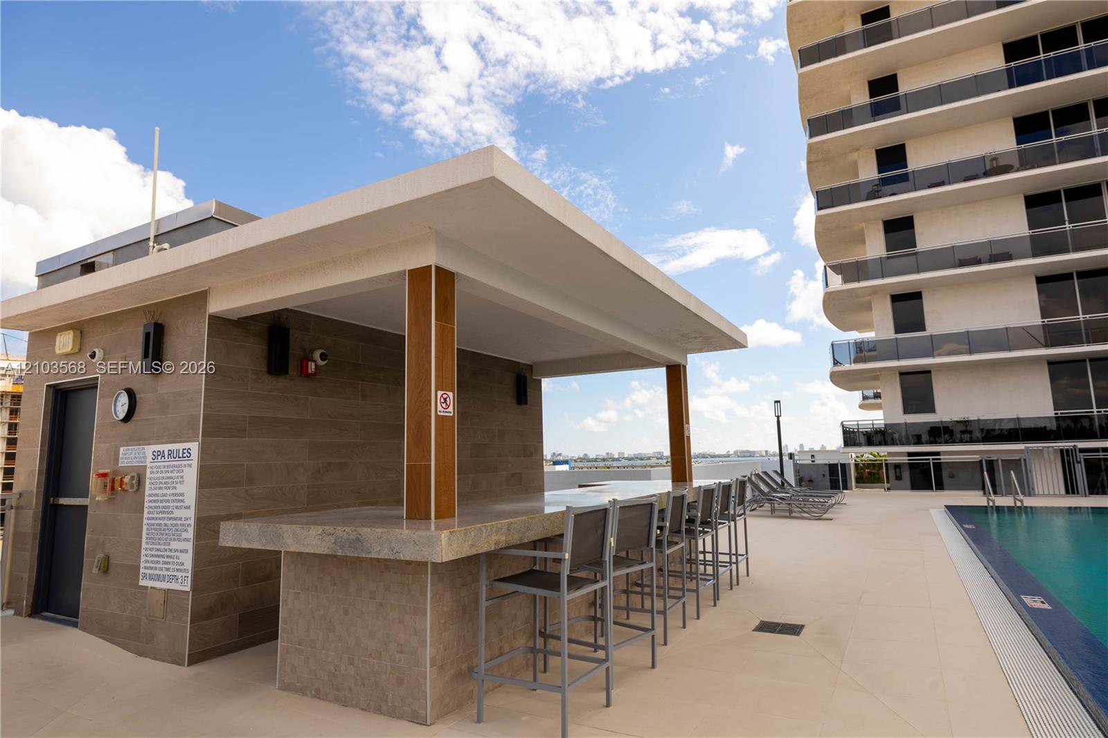 Covered outdoor bar featuring tile-clad cabinetry, a stone-finish countertop, and integrated lighting