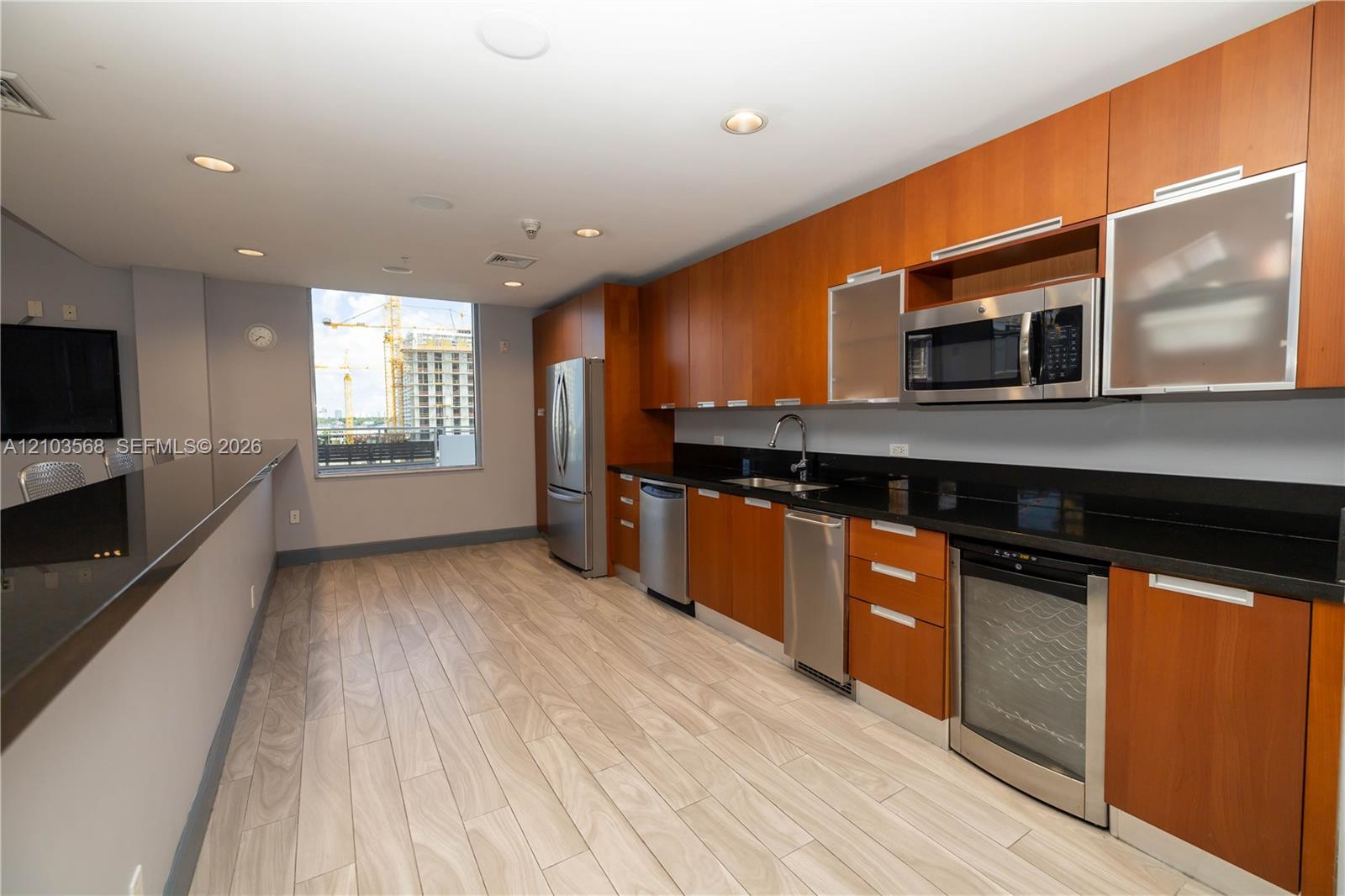 Kitchen featuring flat-panel wood cabinetry, dark solid-surface countertops, built-in stainless steel appliances, a wine refrigerator, and wood-finish tile flooring