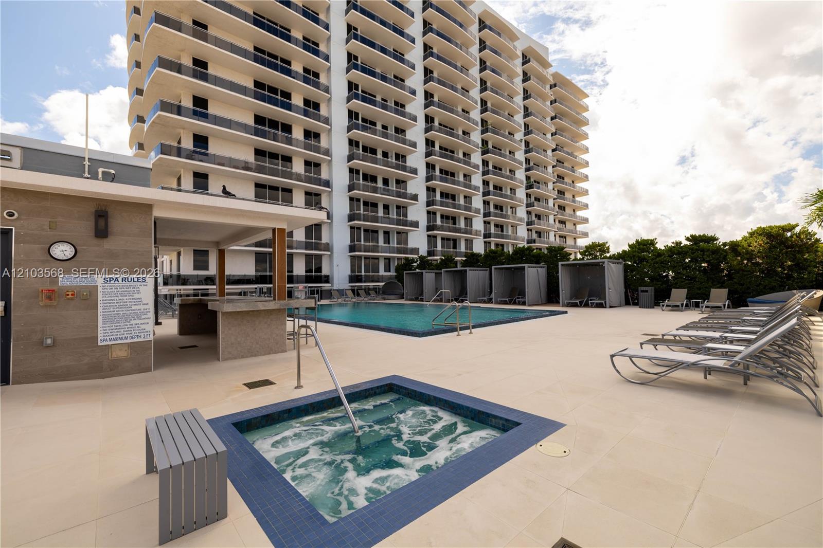 Outdoor recreational area featuring a swimming pool, integrated spa, covered bar with stone-finished counters, and paved sun deck