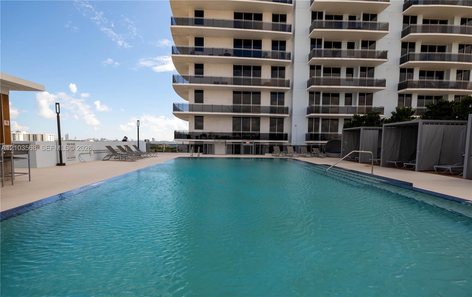 Swimming pool featuring a tiled waterline, metal handrails, and a surrounding deck with built-in poolside cabanas